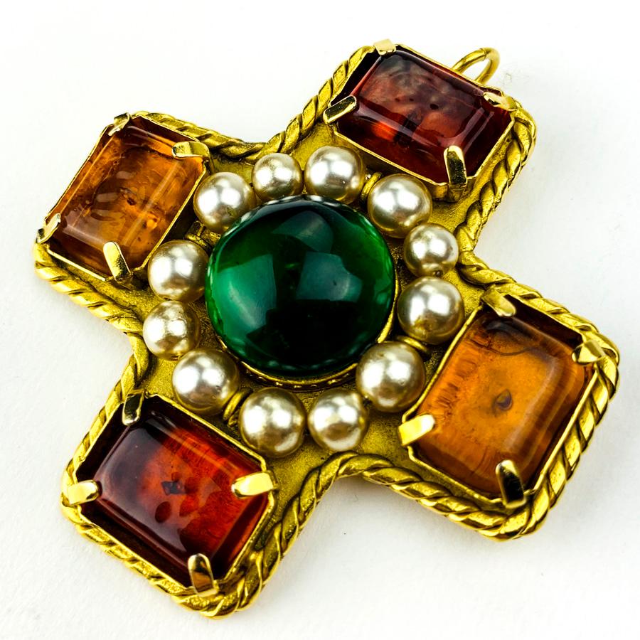 The brooch is a jewel CHANEL. It represents a cross with on each branch a rectangle of glass paste in shades of orange. In its center we discover a ball of green glass paste encircled with pearls.
The brooch is in good condition. Only a few chips on