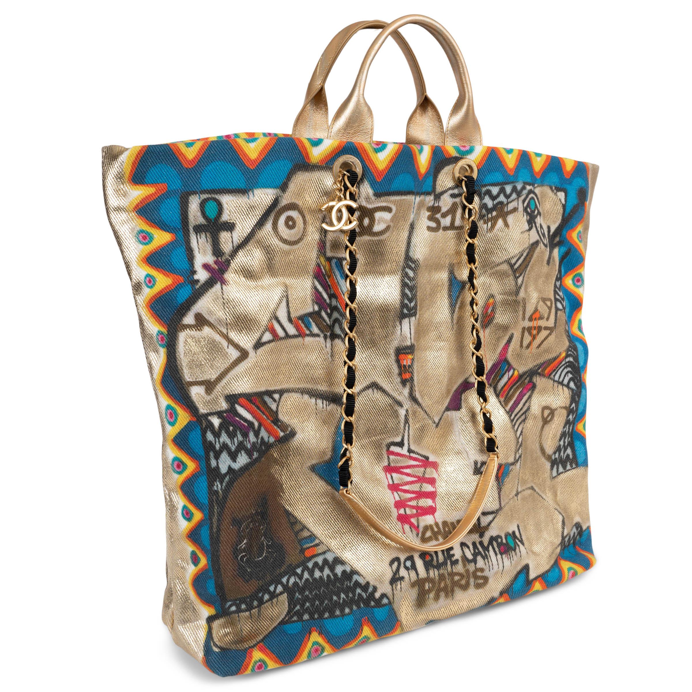 This 100% authentic Chanel Street Spirit tote in metallic gold canvas is a bold expression of urban artistry, featuring Egyptian-inspired graffiti print in black, blue, red, orange, and yellow. Designed with dual carrying options, it includes short