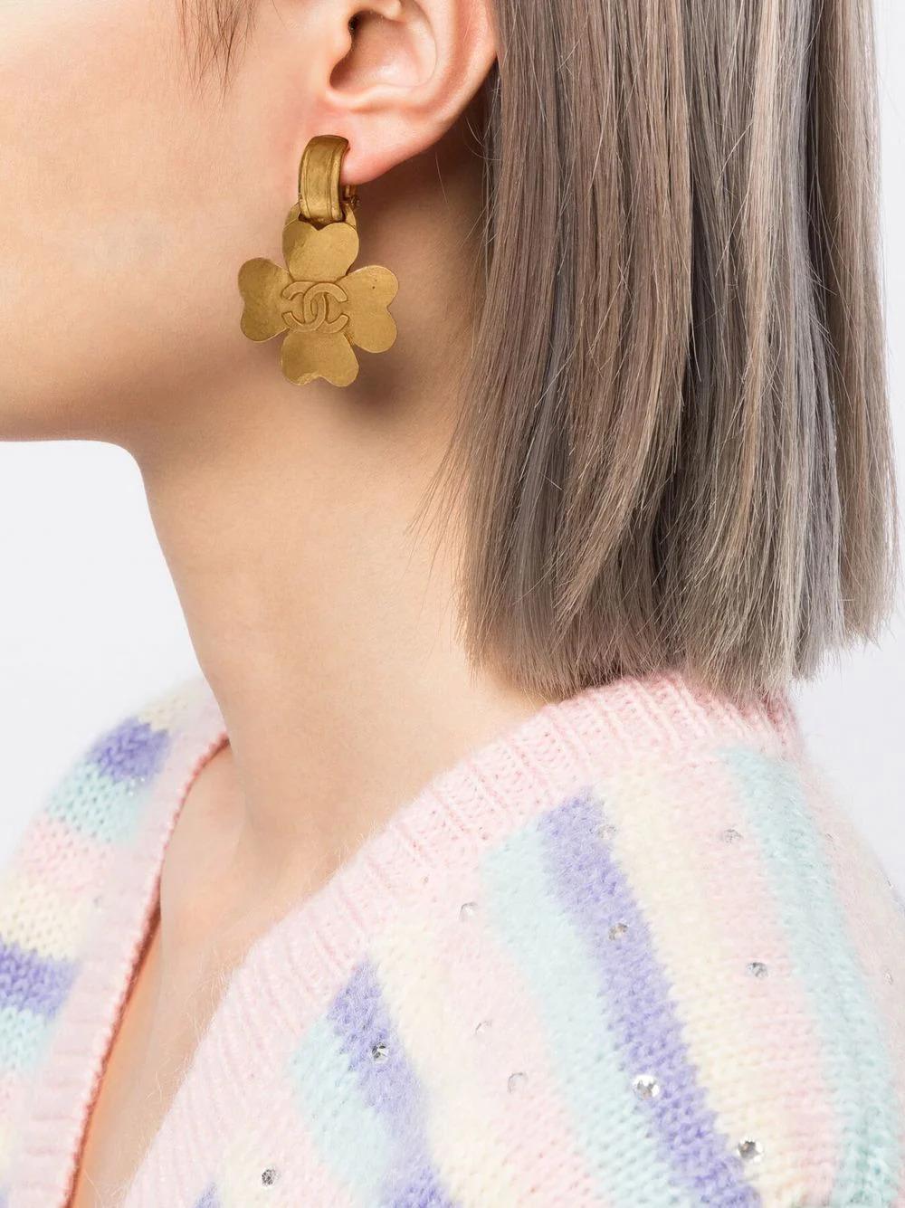 Diese Ohrringe im Vintage-Stil aus dem Jahr 1995 zeigen ein goldfarbenes vierblättriges Kleeblatt, das an einem kleinen Ring hängt und in der Mitte mit einem ineinandergreifenden 