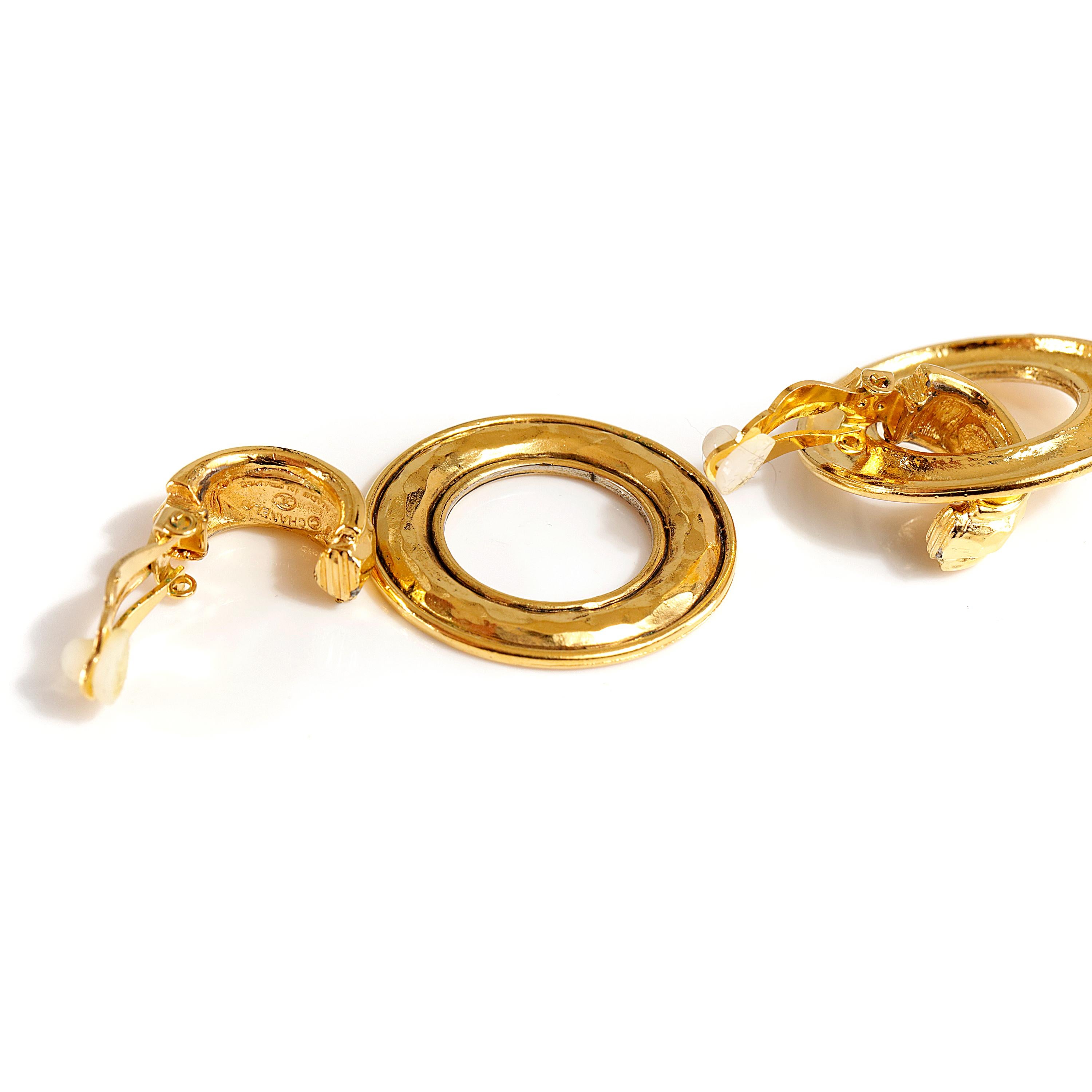 These authentic Chanel Gold Hammered Hoop Earrings are in excellent condition.  Round gold hoop dangles from a small demi hoop.  Intentionally hammered texture.   Clip on closure. Made in France. 


