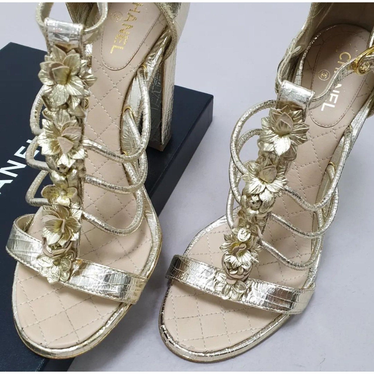 ¡Sal a la calle con estilo con estas impresionantes sandalias Chanel! Confeccionadas en piel con textura dorada metalizada, estas sandalias presentan un delicado detalle de camelia y una elegante tira en el tobillo. Perfecto para añadir un toque de
