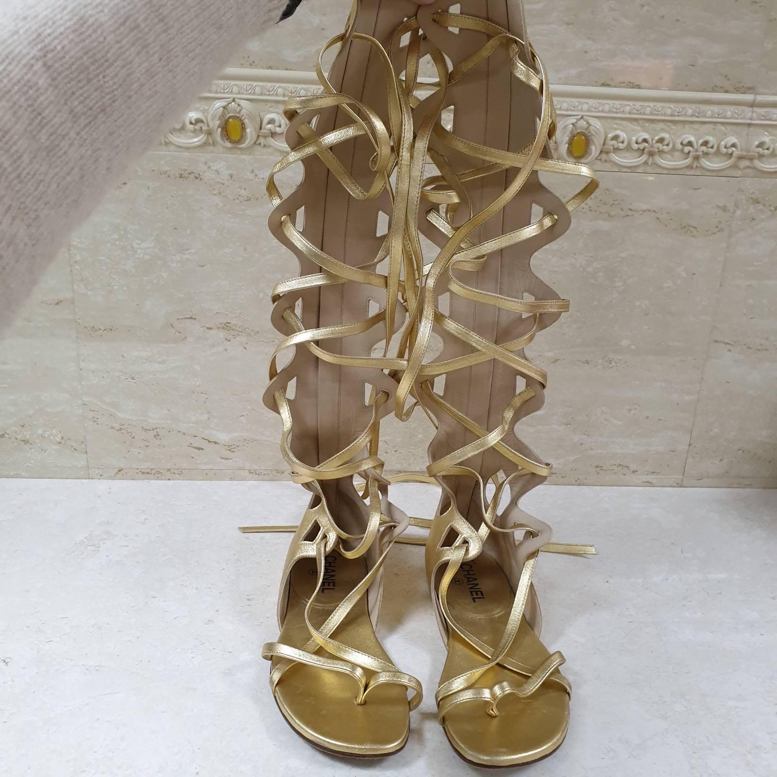 This is an authentic pair of CHANEL Metallic Lambskin Gladiator Sandals 
Sz.38 in Gold. 
This chic pair of gladiator sandals is crafted of gold calfskin leather. 
The sandals feature a 17.5 inch lace up shaft with criss cross vamp straps and gold