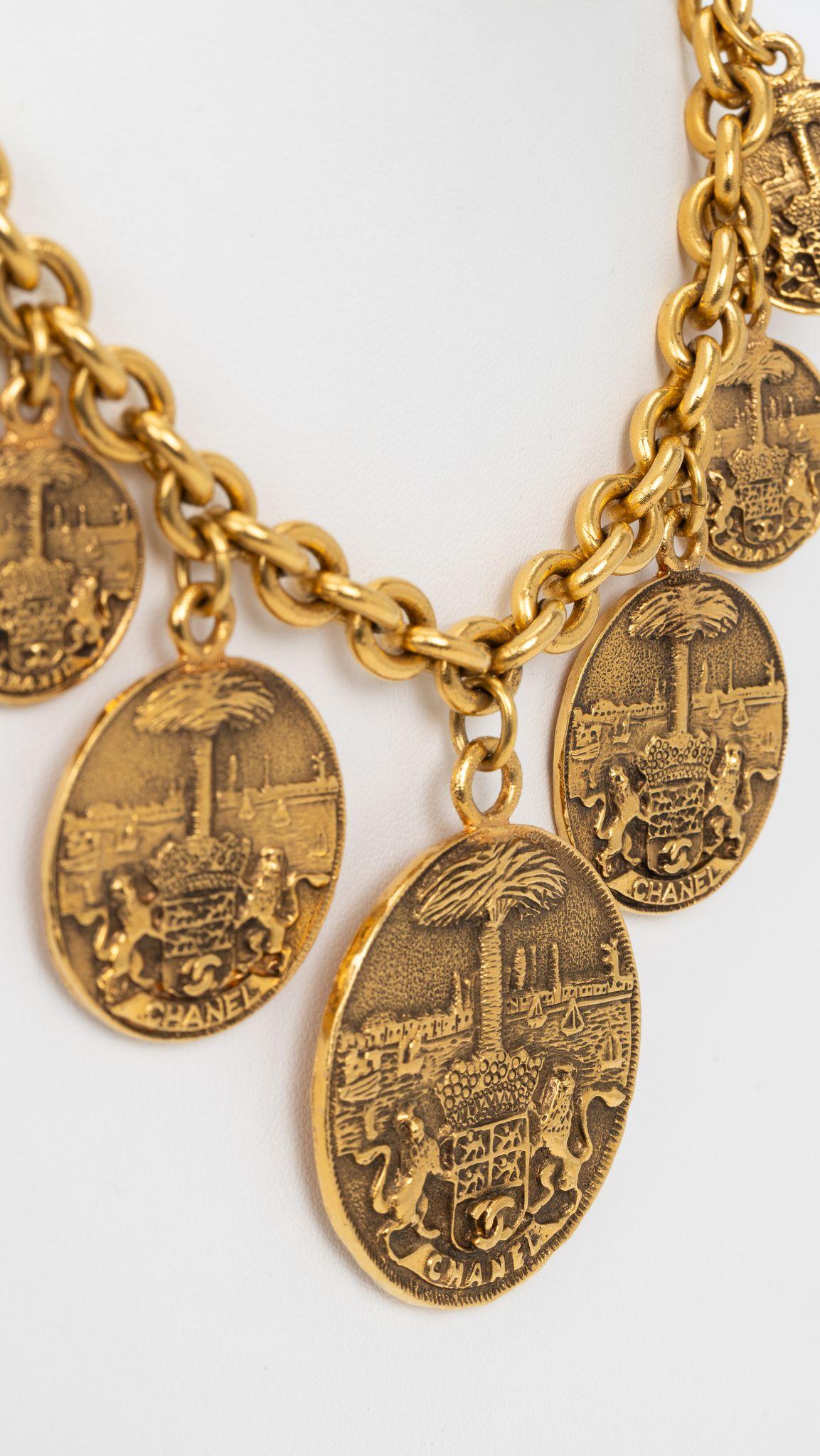 Chanel Gold Medallion Coat of Arms Crest Lion Necklace. Gold toned medallions are engraved of seaside view with sailboats on water and palm tree in center and two lions with CC Breast. 7 medallions. Center pendant. D 2.2” x 1.75”. 80s collection.