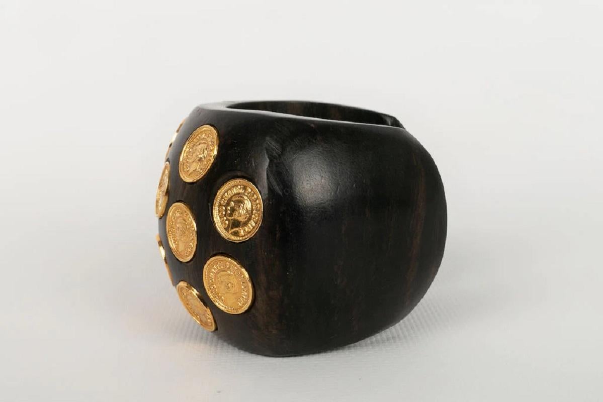 Chanel -(Made in France) Wooden bracelet paved with gold metal coins featuring the profile of coconut. Collection 2cc8. To note, slight wear of the wood.

Additional information:
Dimensions: Circumference: 12 cm 
Opening: 3 cm 
Height: 5.5