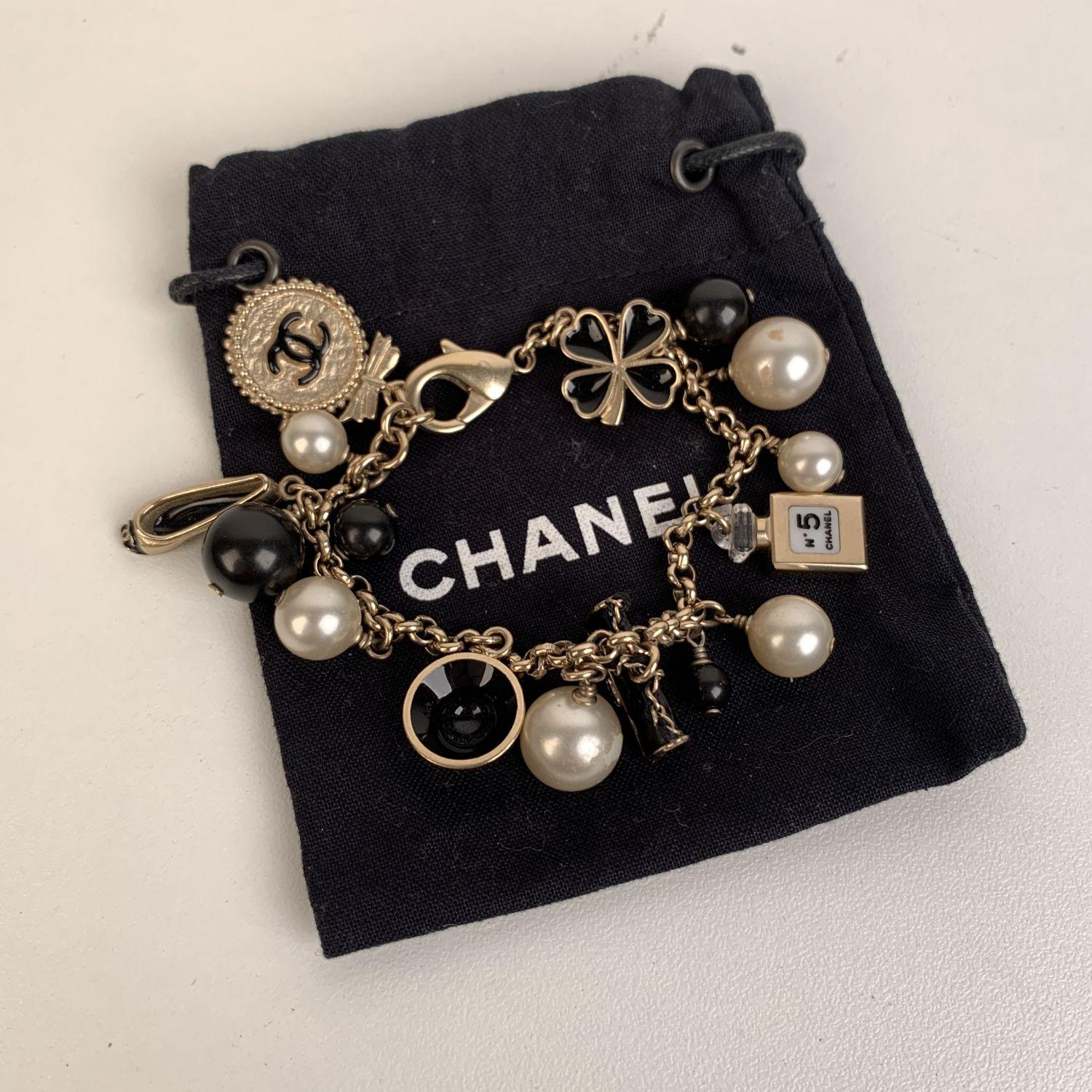 Lovely charms bracelet by CHANEL. Gold metal chain, faux pearls, black beads and iconic Chanel charms (a logo medallion, a bag, a hat, a ballet flat, a clover and a bottle of perfume). Lobster closure. Stamped 'CHANEL - B12 CC A - MADE IN ITALY'