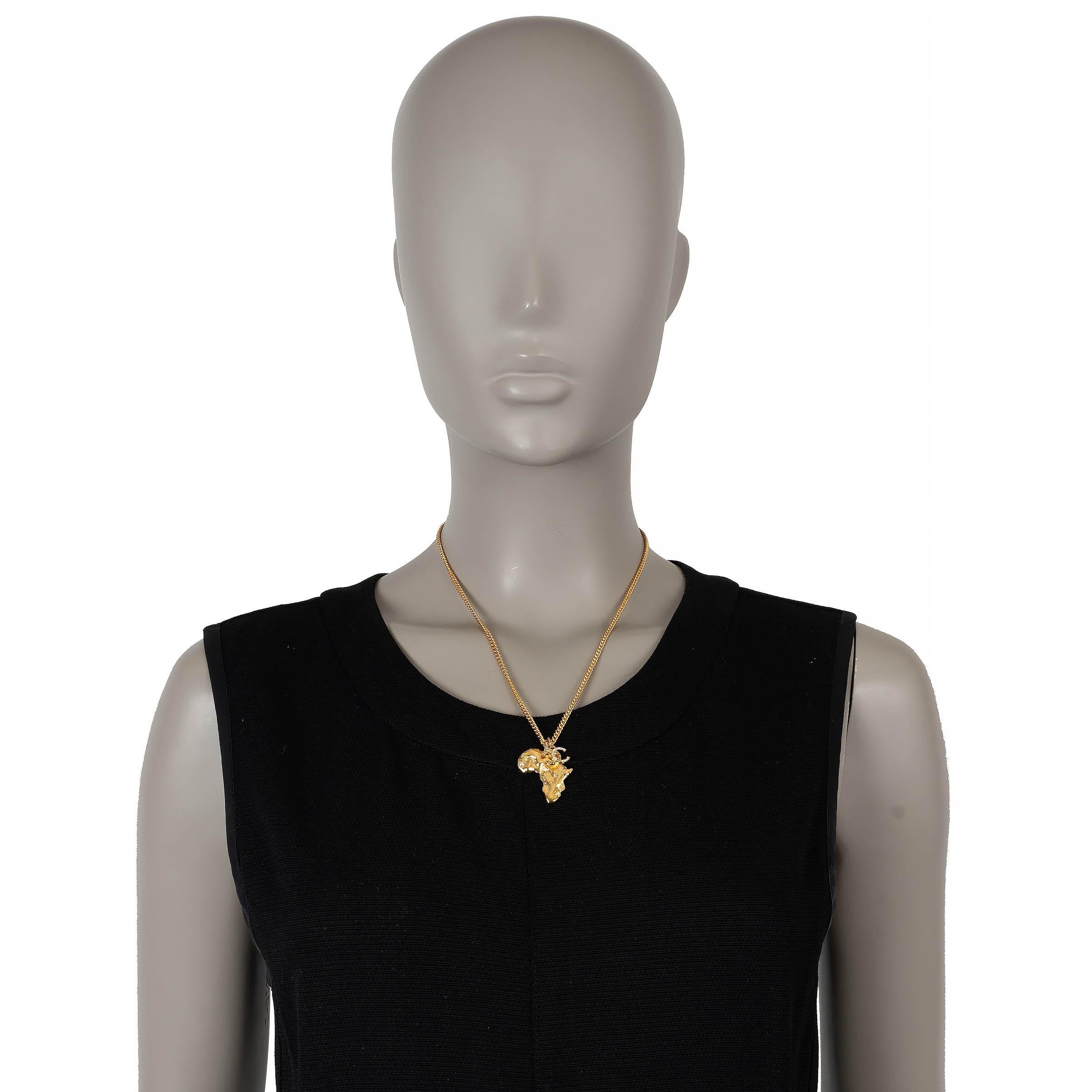 Este collar de cadena 100% auténtico de Chanel en metal dorado es un llamativo homenaje a la elegancia cultural. Con un colgante en forma de África, está adornado con una perla de resina blanca nacarada que marca la ubicación de Dakar y una CC