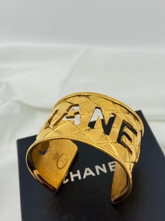 CHANEL Brazalete acolchado dorado con logotipo recortado, Años 80