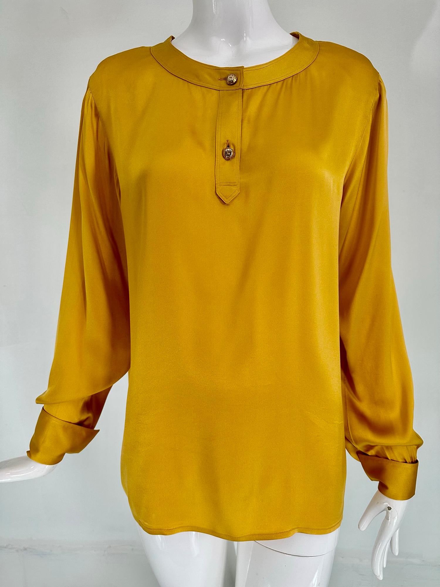 Chanel goldfarbene Seidensatin-Bluse mit flachem Kragen und langen Ärmeln aus den 1990er Jahren. Schöne Seidensatinbluse mit Knopfleiste und zwei goldenen Chanel-Logoknöpfen. Die langen Ärmel haben französische Manschetten, Sie benötigen