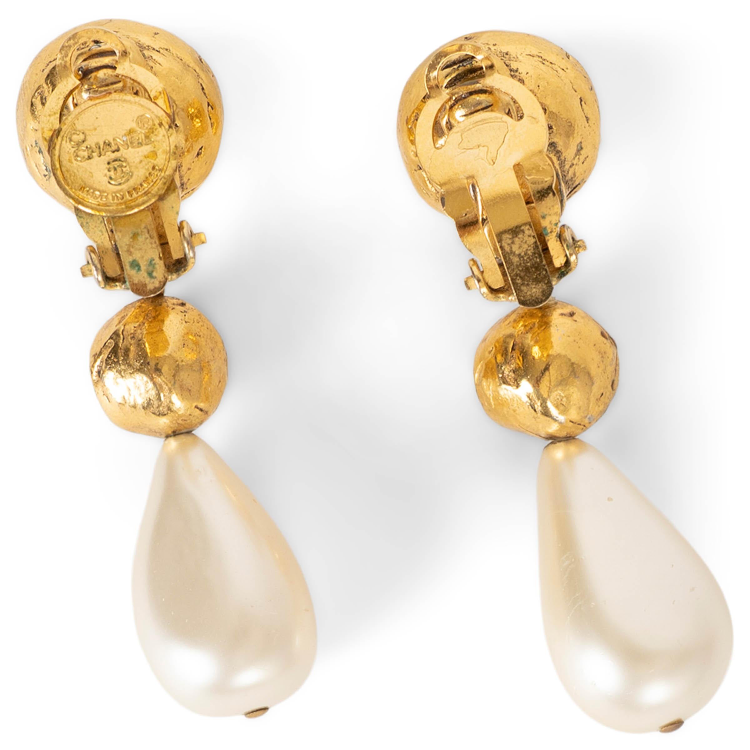 100% authentic Chanel clip-on earrings in gold-tone metal, designed with a sculptural double-ball silhouette. Each earring features a faceted clear rhinestone set into a textured dome, followed by a smaller coordinating sphere suspending a luminous