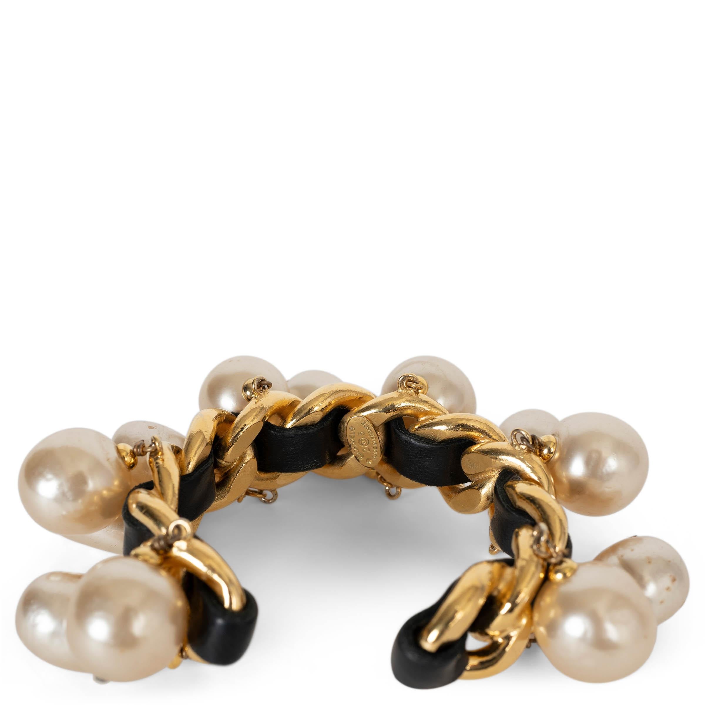 This 100% authentic Chanel cuff bracelet is crafted in gold-plated metal with a chunky chain silhouette interwoven with black leather—an iconic house signature. The bracelet is adorned with oversized pearly white imitation drop-shaped and round