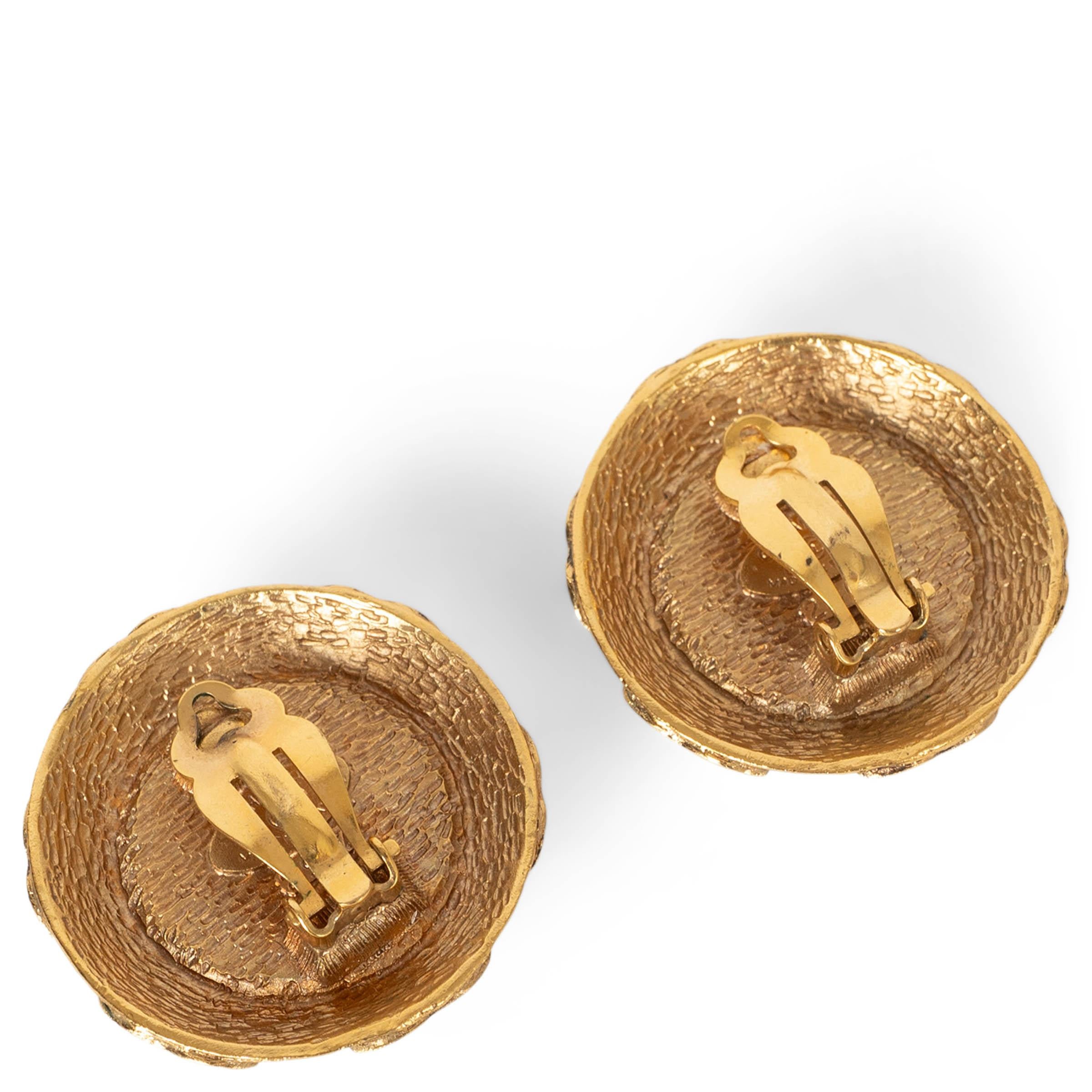 These 100% authentic Chanel clip-on earrings feature a luminous pearly white imitation pearl cabochon framed by a sculpted gold-tone bezel adorned with interlocking CC motifs. A classic and collectible Chanel design that brings elegant signature