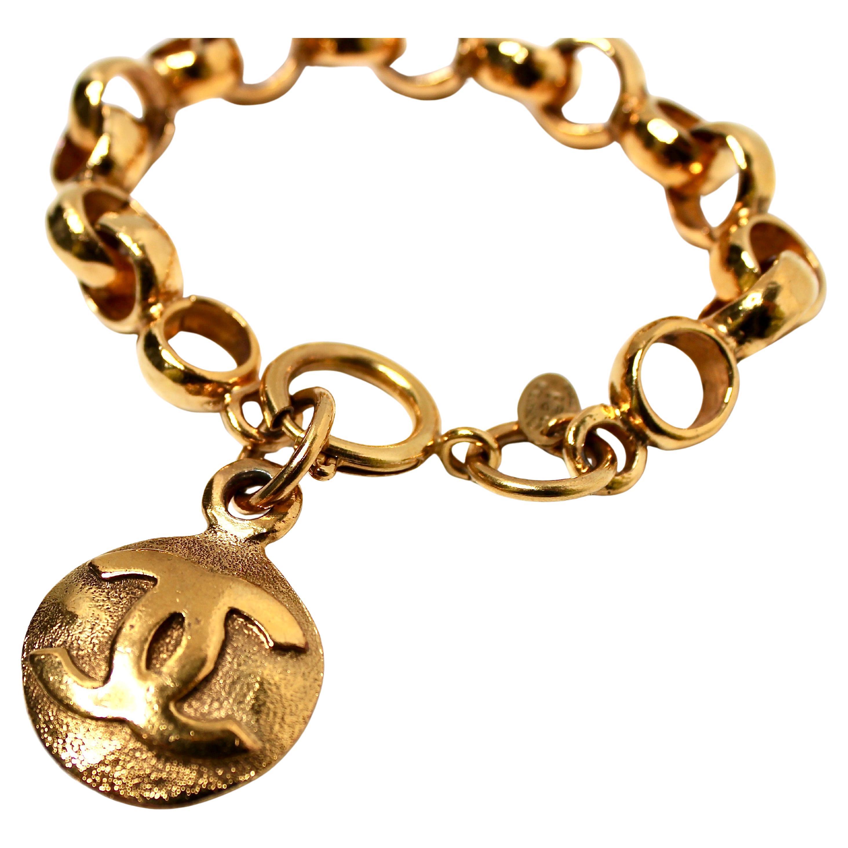 Il bracciale a catena Chanel in tonalità oro con charm CC a incastro degli anni '90 emana un'eleganza senza tempo e un fascino sofisticato. Realizzato con una lussuosa finitura dorata, presenta un audace design a catena che incarna l'iconica