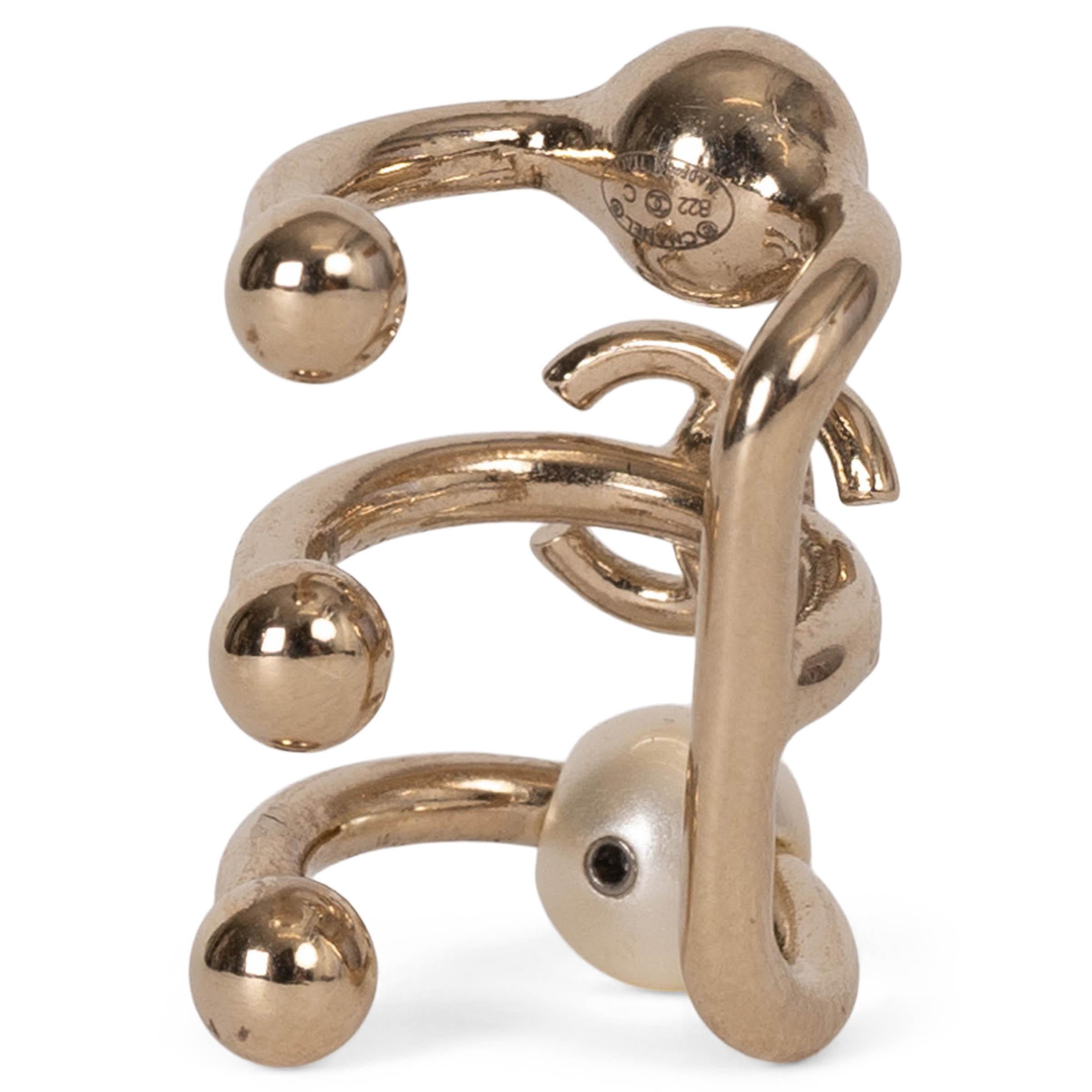 This 100% authentic Chanel CC Pearl & Crystal Ear Cuff in gold is a standout piece, showcasing the iconic CC logo at its center. Adorned with a single pearl and a single crystal, it exudes a refined elegance that adds a glamorous finish to any look.
