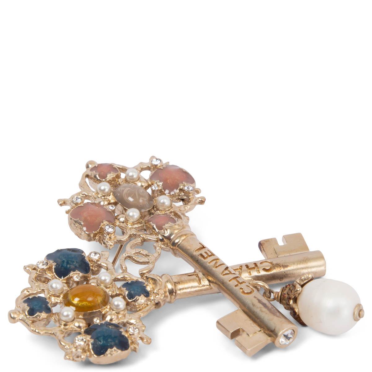 100% authentic Chanel 2017 Metiers d'Art Cosmopolite keys brooch in light gold-tone metal embellished with, blue, nude, taupe and beige stones a dangling faux pearl, small faux pearls and rhinestones. Has been worn and is in excellent condition.