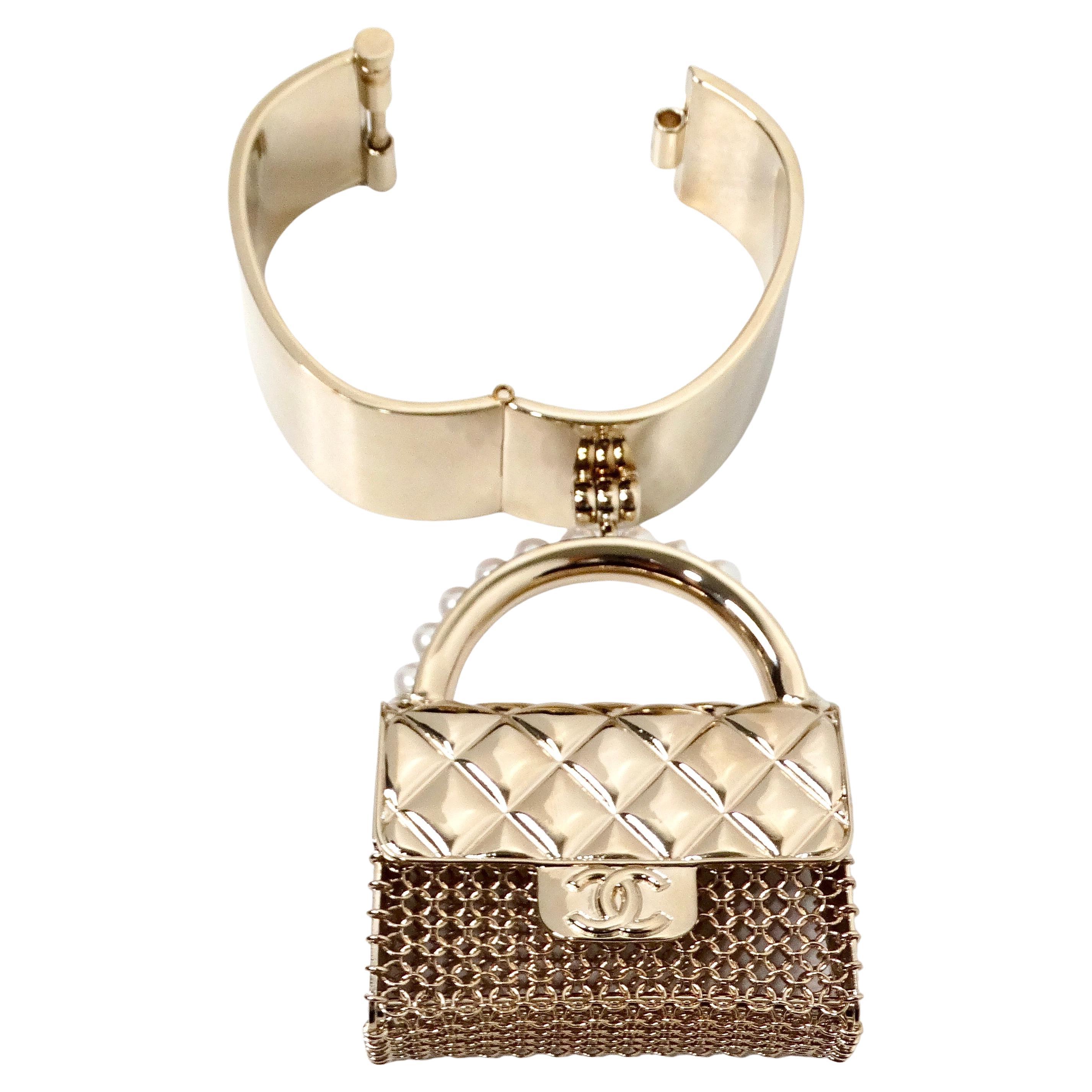 The Chanel Gold-Tone Purse Charm Cuff Bracelet 2021 is an elegant and versatile accessory that embodies the timeless sophistication of the Chanel brand. Crafted in a striking gold-tone finish, this cuff bracelet features a charming flap bag purse