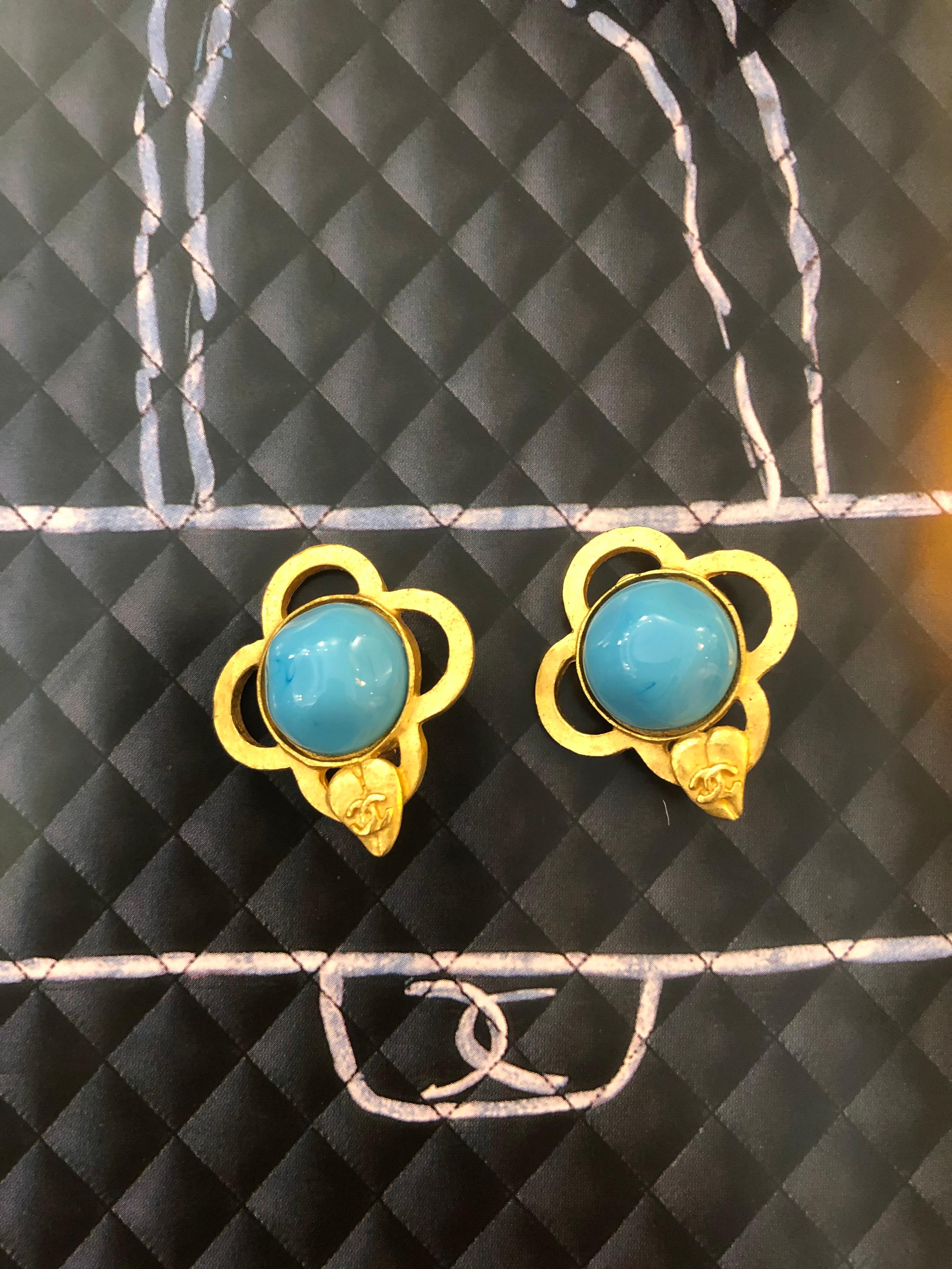 These 1990s Chanel gold toned clover earclips are crafted of gold toned metal set in the shape of clover leaf and adorned with blue colored gripoix in the middle. Rare color amongst Chanel gripoix jewelry. Stamped Chanel 96P, made in France.