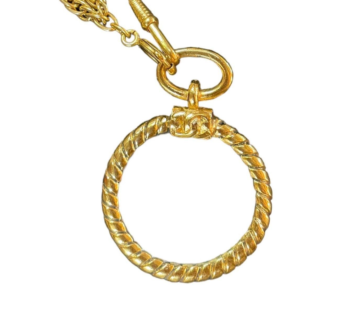 Ajoutez une touche de luxe à votre collection de bijoux avec ce collier Chanel à double brin. Dotée d'une chaîne de montre et d'une loupe en verre au look unique, cette pièce est à la fois fonctionnelle et élégante. Le logo emblématique du double C