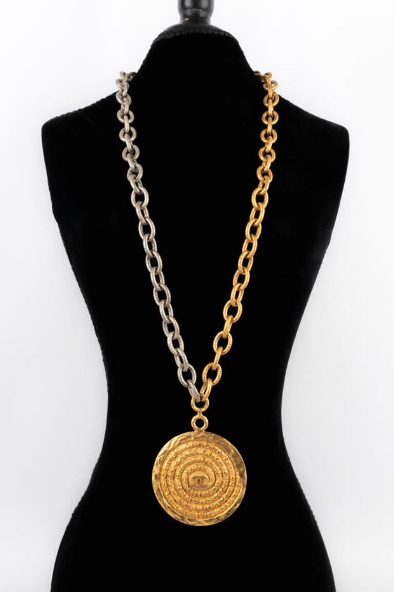 Chanel - (Made in France) Collier chaîne en métal doré et argenté avec un pendentif circulaire battu et gravé. Collectional printemps-été 1993.

Informations complémentaires : 
Condit : Très bon état.
Dimensions : Longueur : 102 cm - Diamètre du