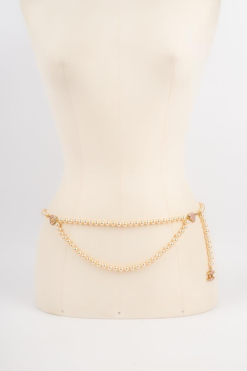 CHANEL - (Made in France) Cinturón de metal dorado y perlas de fantasía adornado con brillantes rosas. Colección Primavera-Verano 2002. Cabe mencionar que algunas perlas están dañadas.

Más información:
Estado: Buen estado
Dimensiones: Longitud: 94