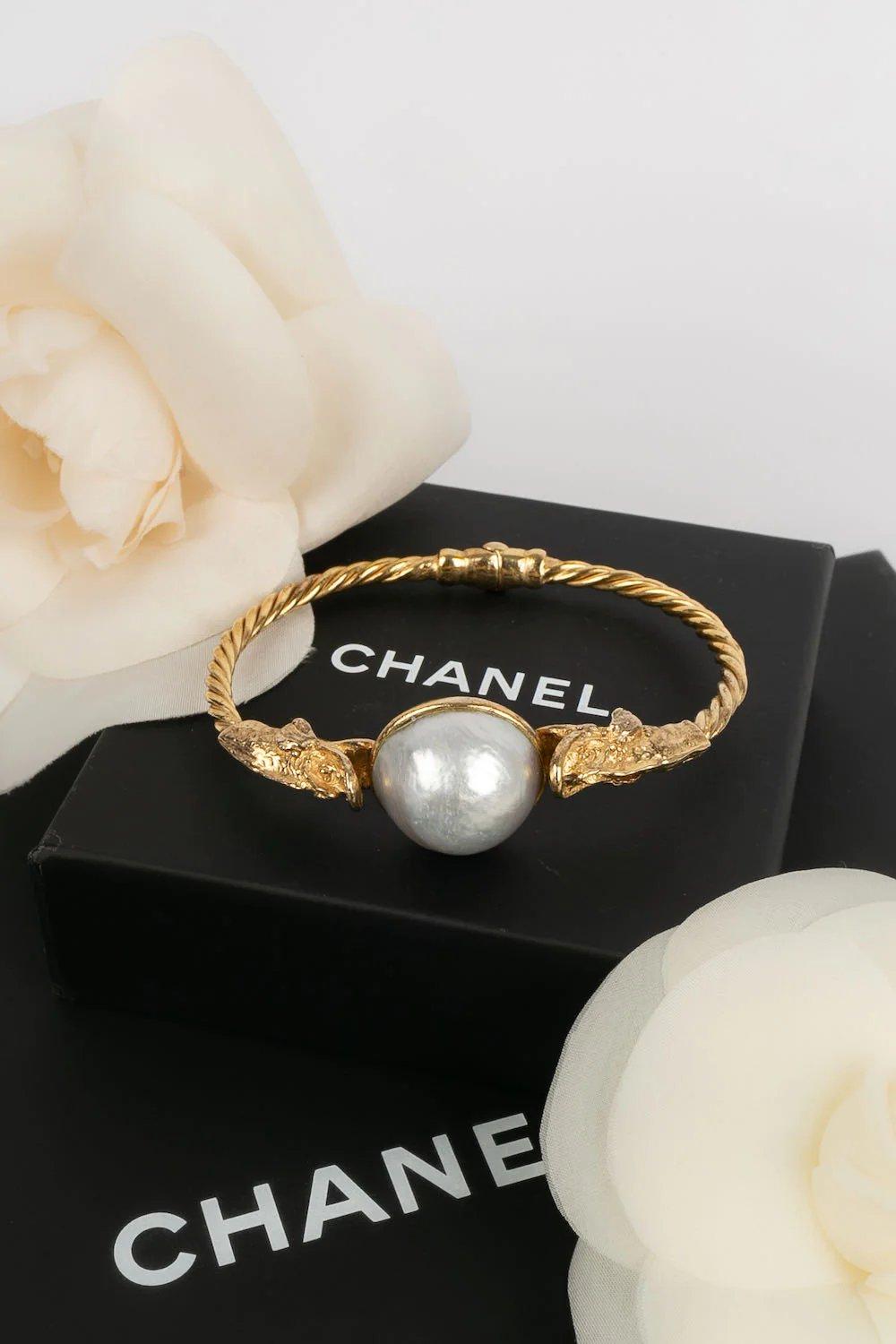Chanel -Golden metal bracelet with pearly cabochon.

Additional information:
Dimensions: Circumference: 19 cm 
Opening: 9 cm
Condition: Very good condition
Seller Ref number: BRAB55