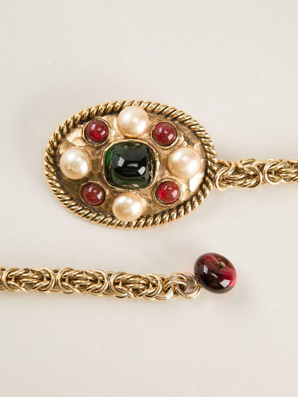 Important Chanel gold-tone pearl embellished chain belt. It features an oval medallion as a buckle, with an emerald green stone at the centre, four small pearls around it, alternated with four small red glass stones. Hook closure. The item is