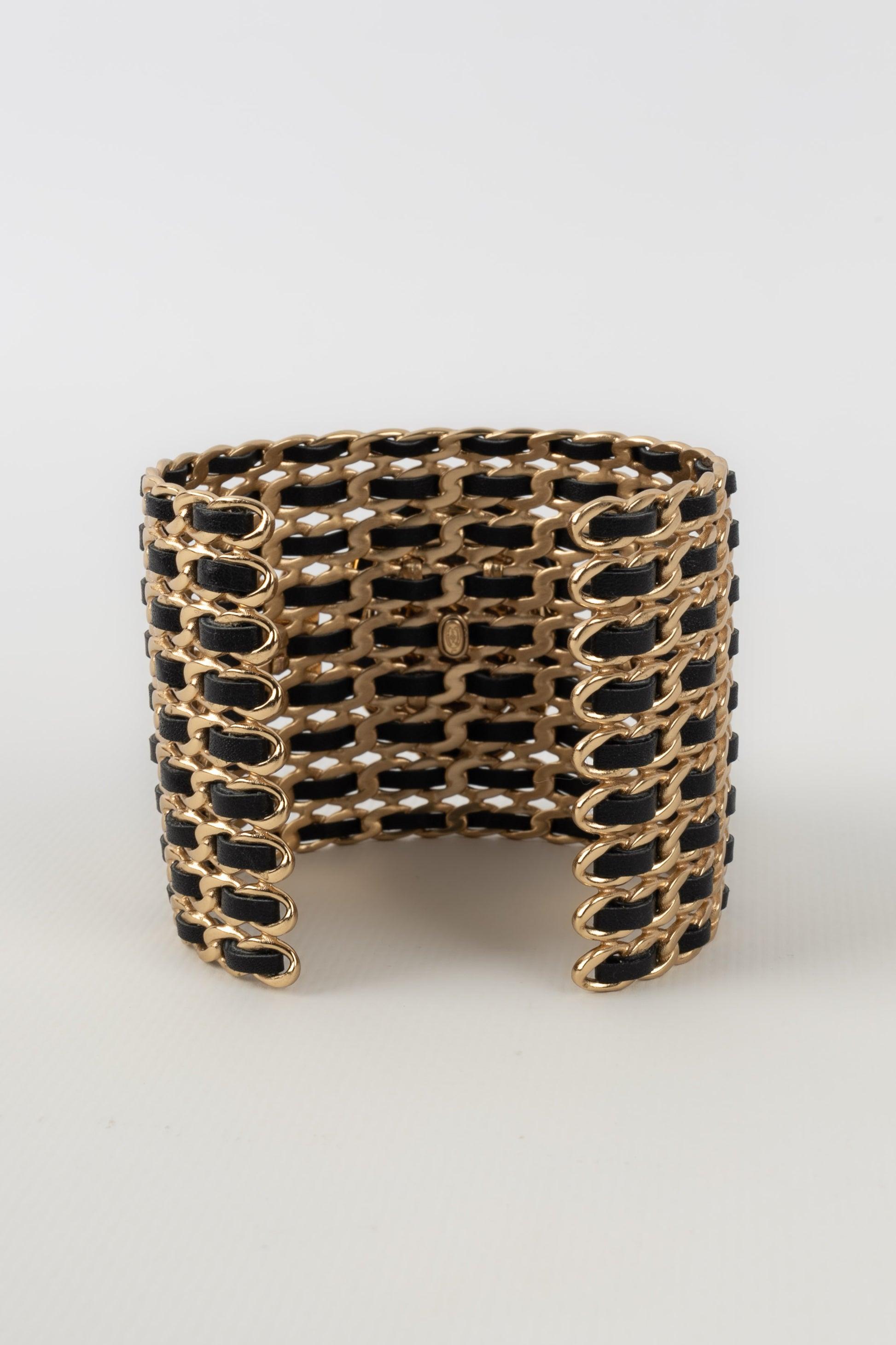 Chanel - (Made in France) Golden metal cuff bracelet interlaced with black leather and topped with an impressive transparent rhinestone. 2022 Collection.

Additional information:
Condition: Very good condition
Dimensions: Length: 15 cm - Opening: 3