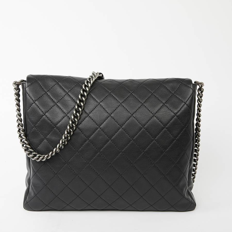 This CHANEL satchel is in black grained calfskin lined with fabric. It closes with a large flap, with a very practical inside, a large storage space for files and computer and a zipped pocket.
The jewelry is in ruthenium aged silver metal, on the