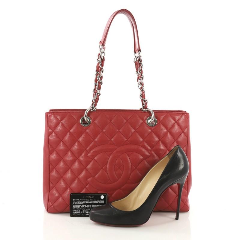 This Chanel Grand Shopping Tote Quilted Caviar, crafted in red quilted caviar leather, features woven-in leather chain straps with leather pads, an exterior back pocket, and silver-tone hardware. It opens to a gray satin interior with two open