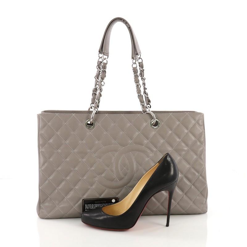 This Chanel Grand Shopping Tote Quilted Caviar XL, crafted in gray quilted caviar leather, features a stitched CC logo in the middle, woven-in leather chain straps with leather pads, exterior back pocket, and silver-tone hardware. It opens to a gray