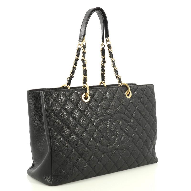 This Chanel Grand Shopping Tote Quilted Caviar XL, crafted in black quilted caviar leather, features woven-in leather chain straps with leather pads, stitched CC logo, exterior back pocket, and gold-tone hardware. It opens to a black satin interior