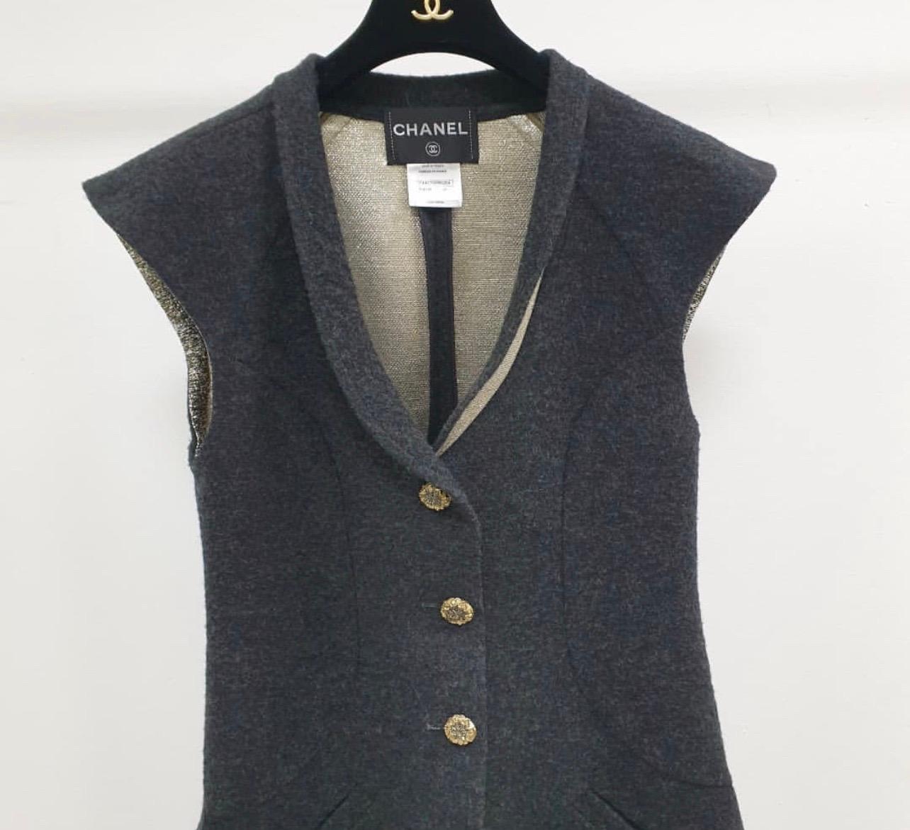 Beautiful Chanel grey silk blend vest-overcoat dress.
 It features a v-neck, a shawl lapel, a front button fastening, cap sleeves, side slit pockets, a flared style, a mid-length, a back buttoned strap and gold-tone and silver-tone flower