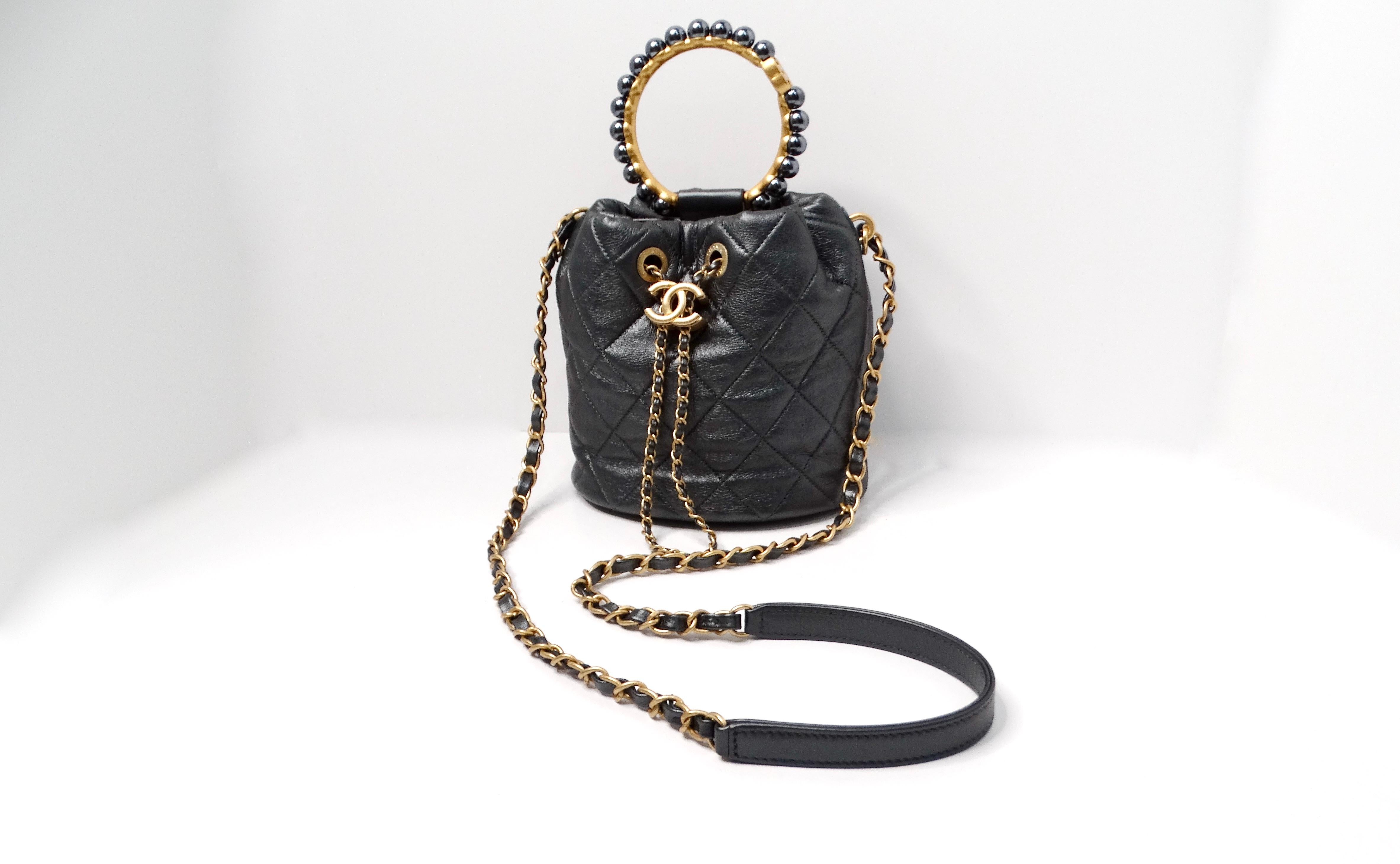 The Chanel Gray Metallic Quilted Lambskin Pearl Crown Drawstring Bucket Bag is a stunning addition to any fashionista's collection. Crafted from soft lambskin leather in a luxurious dark gray metallic hue, this bag exudes elegance and