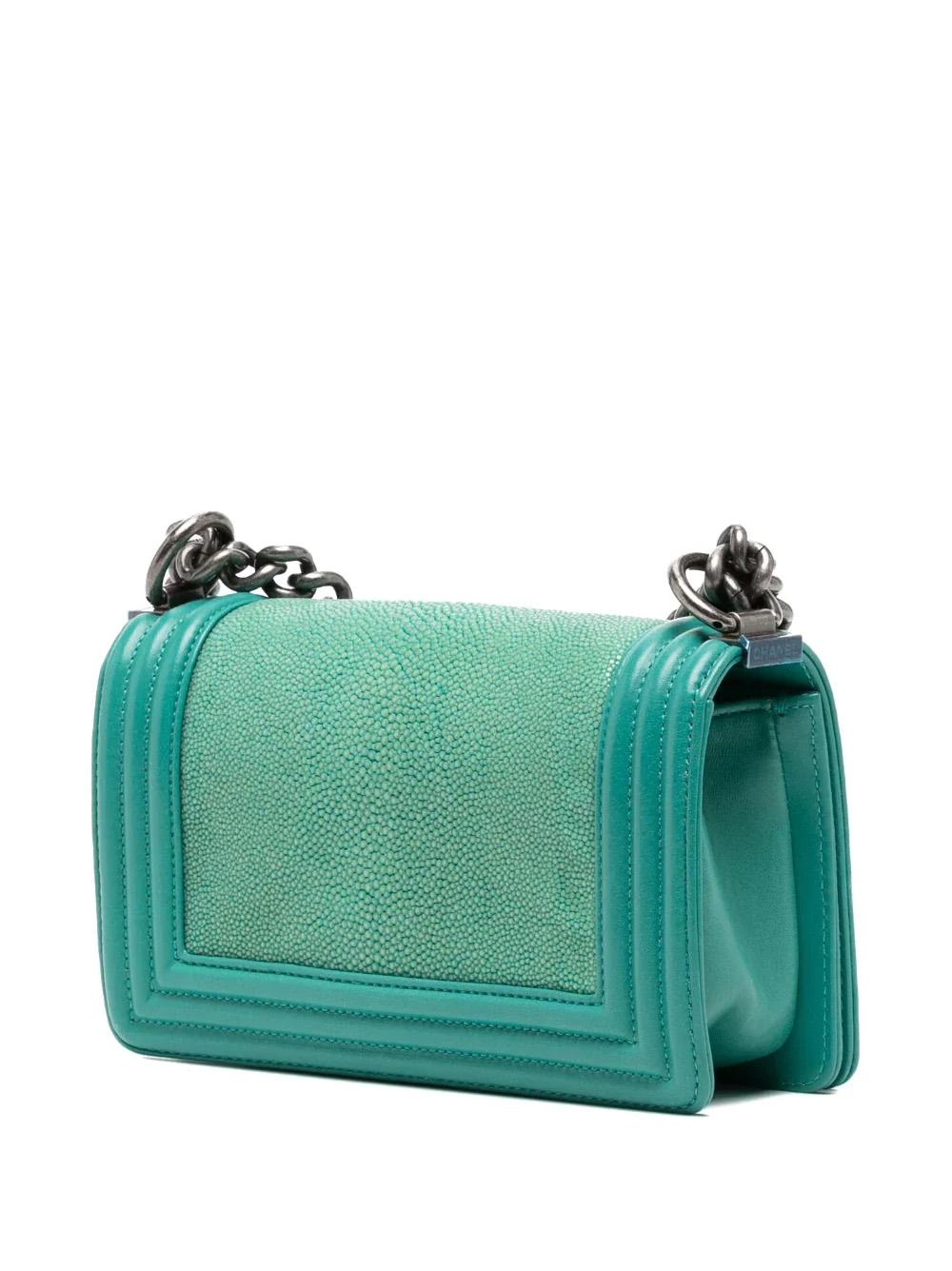 This Small Galuchat Boy Bag is a signature Chanel handbag crafted with 100% leather. Its turquoise blue-green colour is complemented by a shagreen and lambskin finish, featuring a signature gourmet-chain shoulder strap, a front flap closure, a