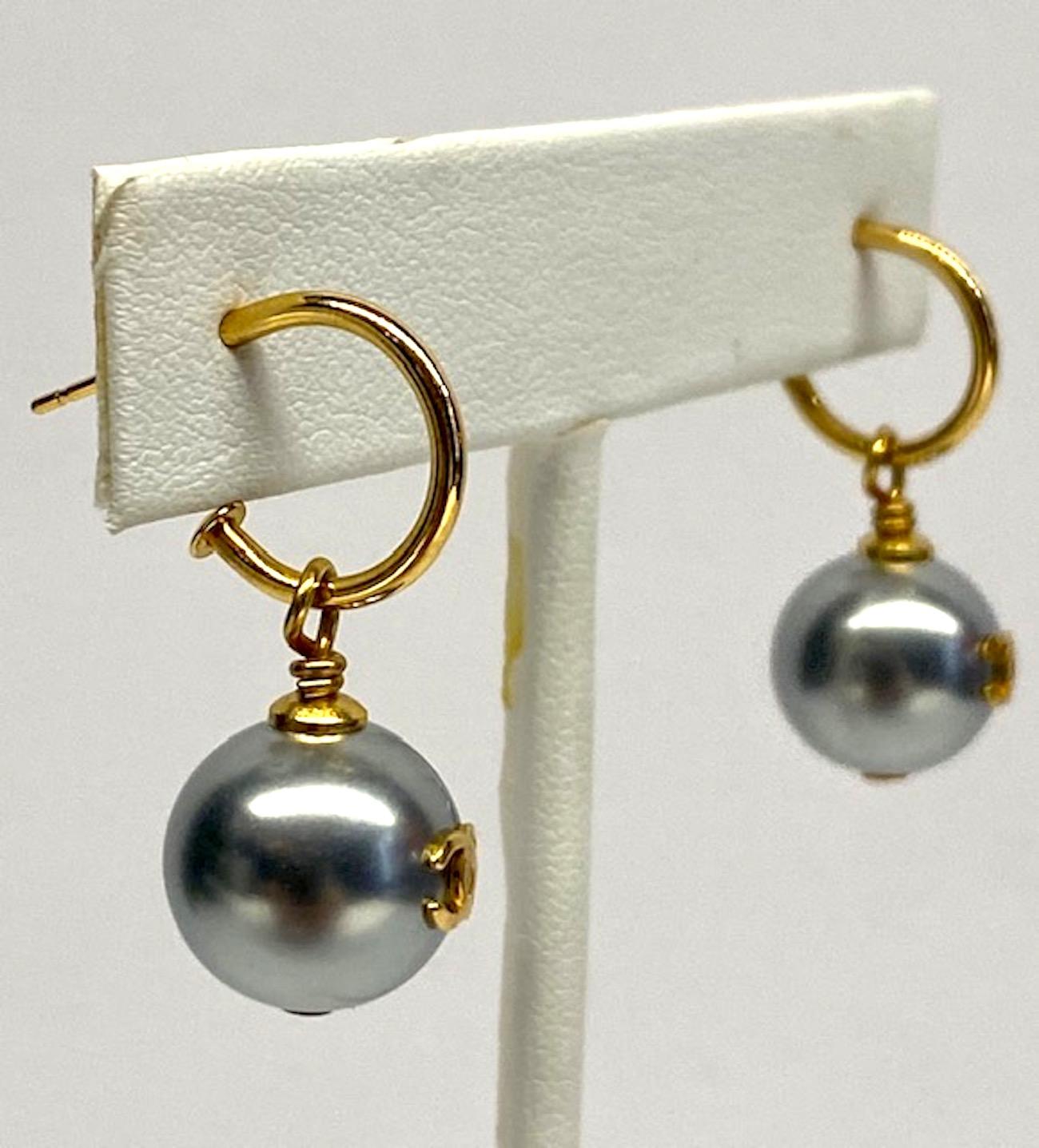 A classic pair of Chanel grey pearl dangle earrings. Each faux pearl is 12 mm (a half inch in diameter) in size, has the iconic Chanel interlocking CC logo in the front and hangs from a shiny gold hoop for pierced ears. The pearl may be removed to