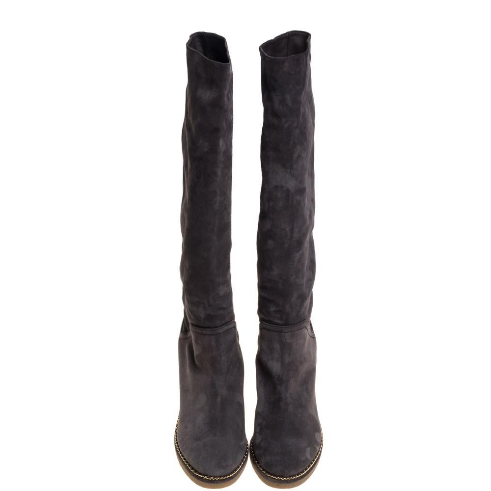 Simple and sophisticated, these knee-length boots from Chanel are a must-buy for the fashionable you. These grey-hued boots are crafted in plush suede and come balanced on platforms and wedge heels. They are detailed with the CC logo and chain-link