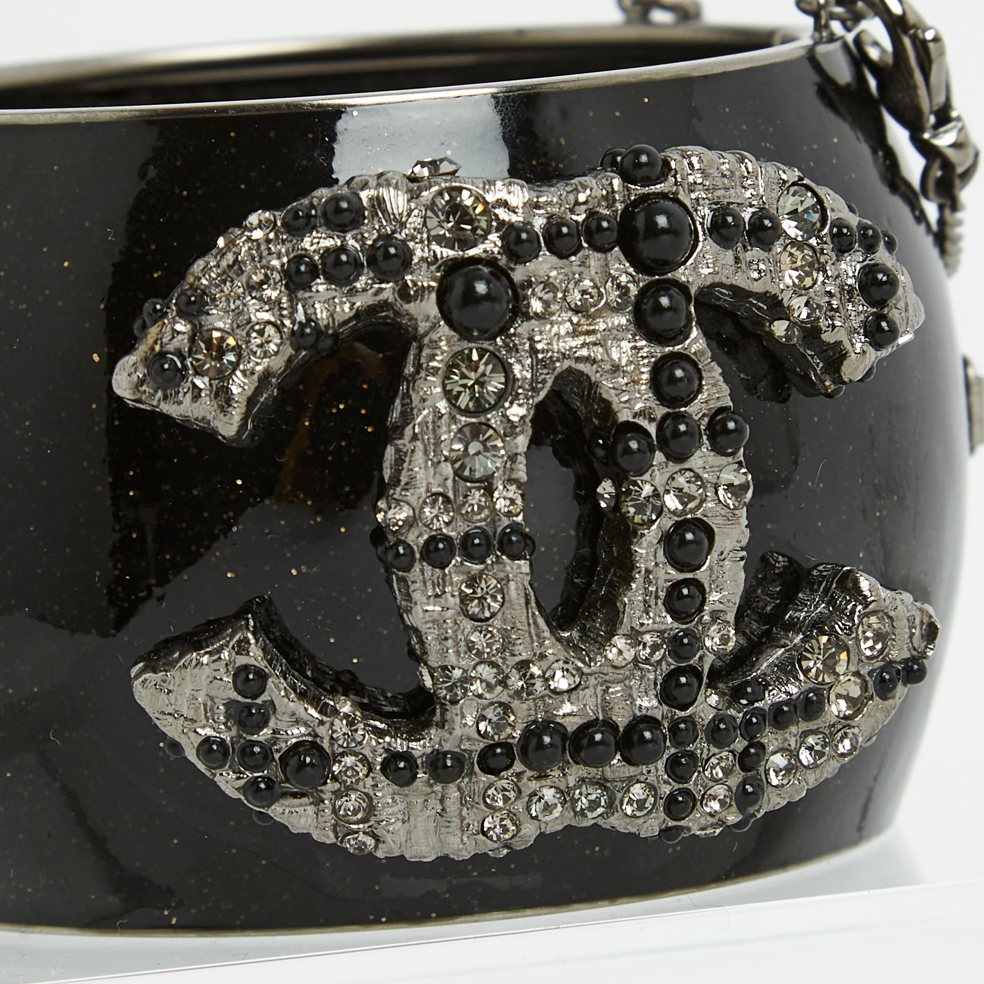 Chanel cuff bracelet in aged silver metal covered with sparkling black enamel with brown reflections topped with a large CC logo in tweed-style metal dotted with rhinestones and cabochons of different sizes and colors, interior lined with quilted