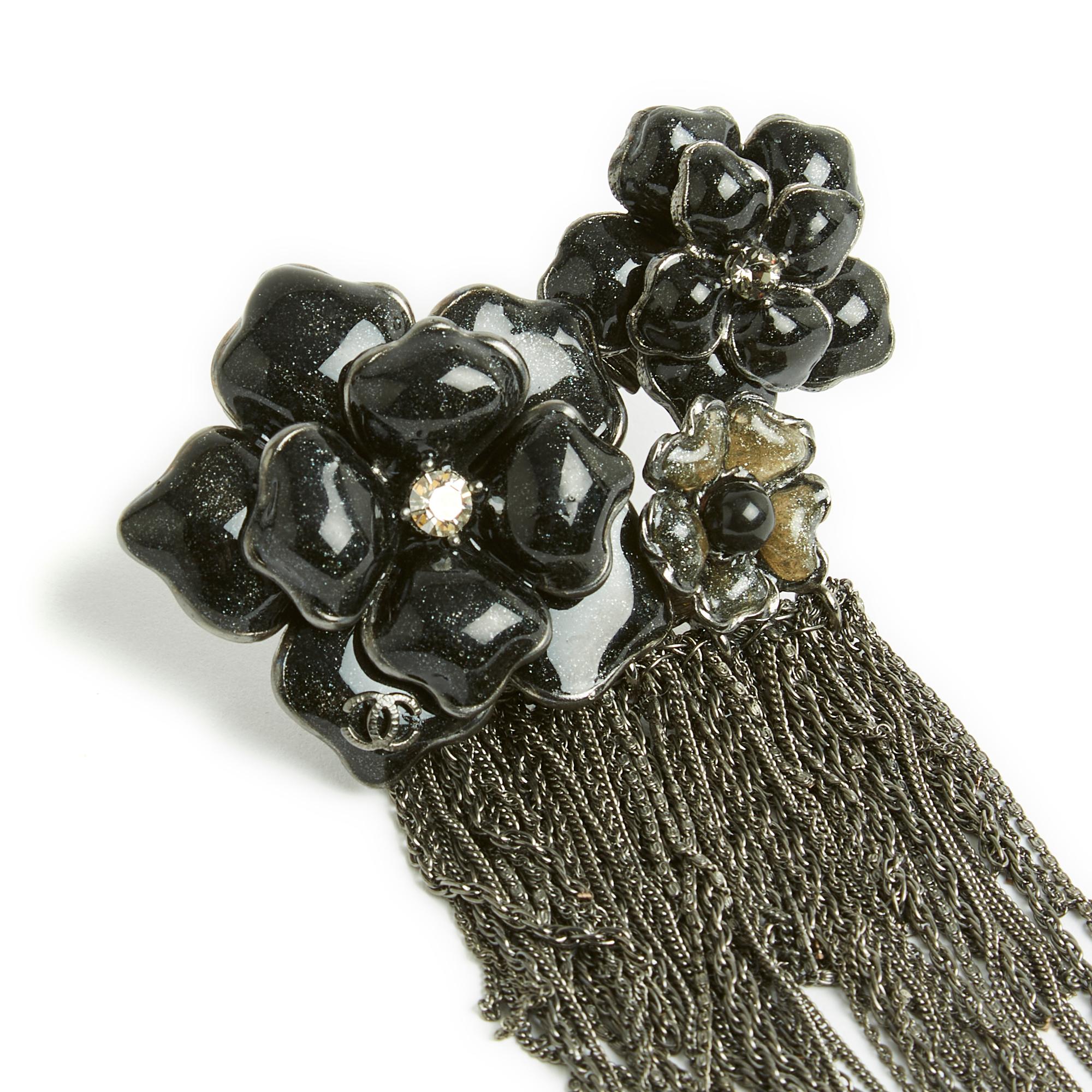 Chanel brooch probably Haute Couture in silver metal composed of 3 camellia flowers in glass paste or black and anthracite gray resin inlaid with sequins and multiple hanging chains. Width 7.4 cm, total length 14 cm. The brooch is in excellent