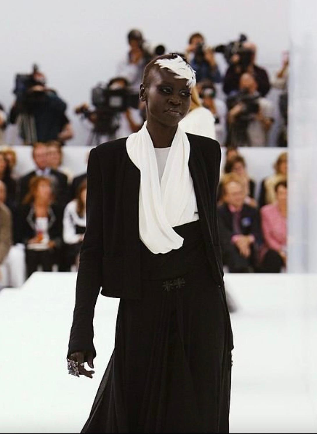 Introducing the iconic Little Black Jacket from Chanel Fall/Winter 2004 Haute Couture collection. Look #44, as seen on model Alek Wek. Boasting an open front, collarless design, and boxy cut, it combines elegance and versatility seamlessly. The