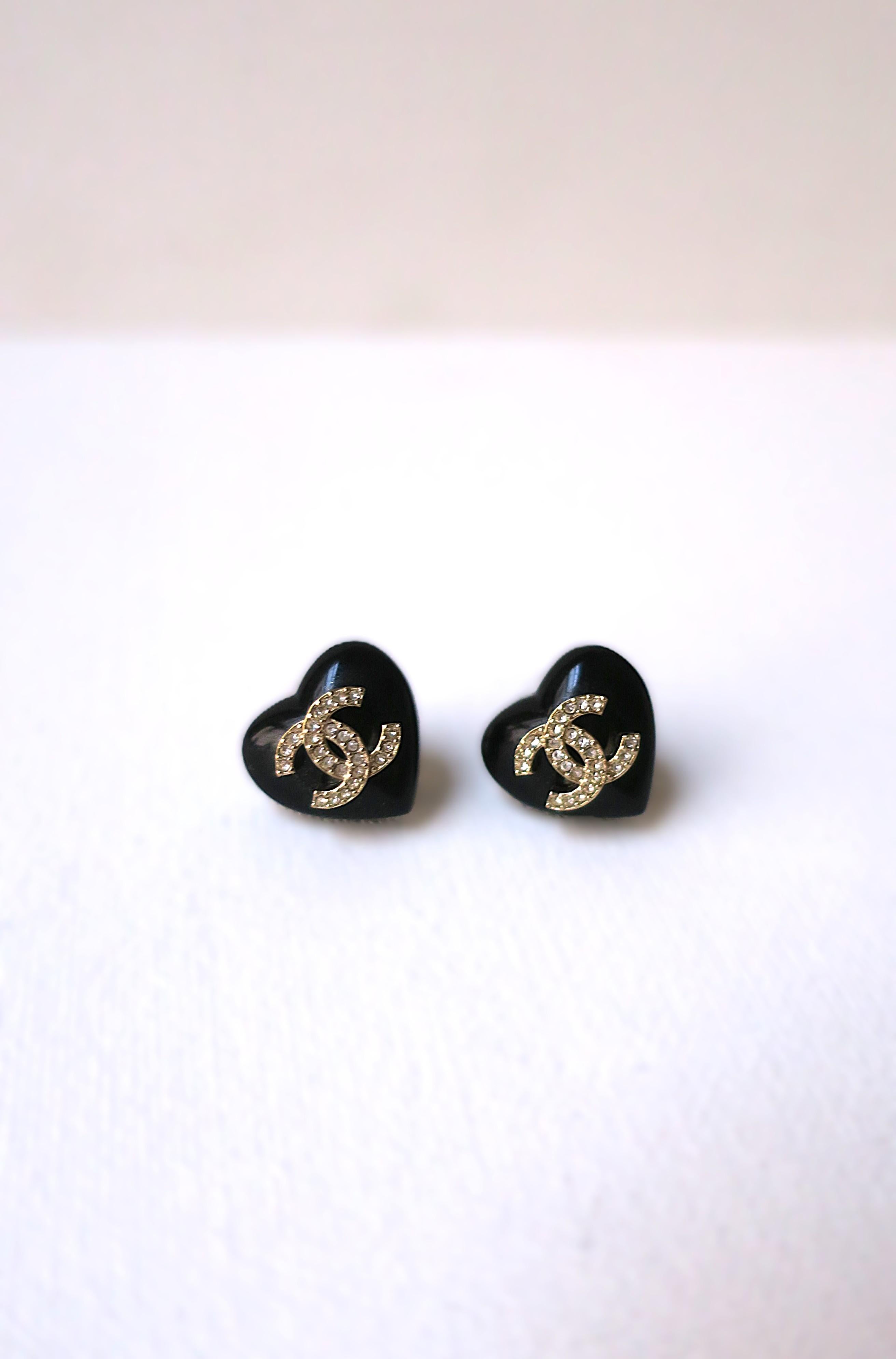 A beautiful and chic pair of black and gold heart earrings from French luxury Maison, Chanel. Earrings are heart shaped in black resin with crystal and gold-tone double interlocking C's, Chanel's iconic signature mark. With original Chanel box,