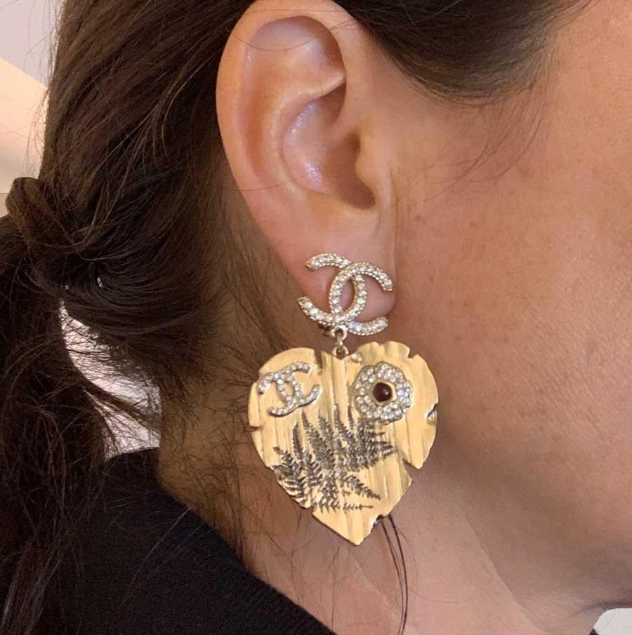 The pair of earrings comes from Maison CHANEL. Each represents a CC set with rhinestones at the end of which hangs a metal heart gilded with fine gold. On each heart come another CC set with rhinestones, as well as a small flower, whose petals are