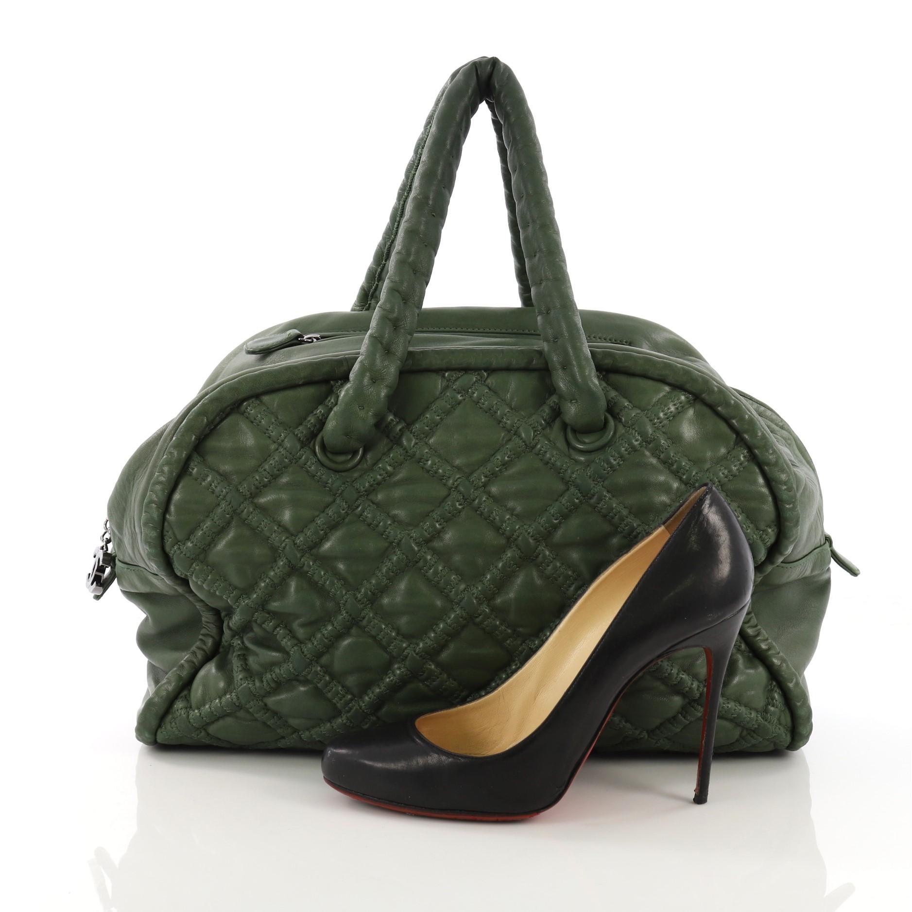 This Chanel Hidden Chain Bowler Quilted Lambskin Large, crafted from green quilted lambskin leather, features dual hidden chain leather handles, CC charm zipper pull, and silver-tone hardware. Its zip closure opens to a gray satin interior with zip