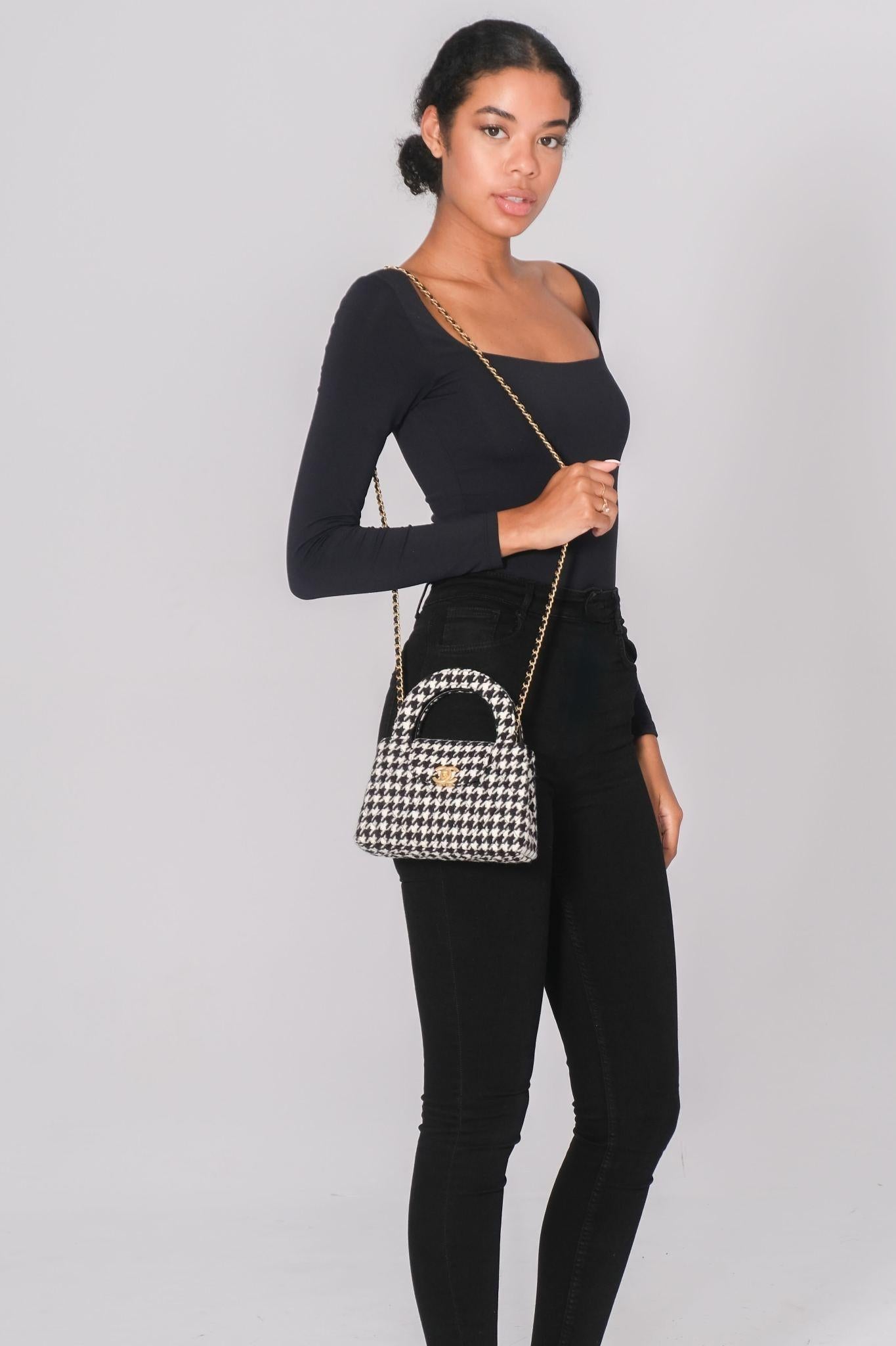 This Chanel Kelly Shopper bag is constructed of black and white tweed in a houndstooth pattern with diamond quilting. It features a front flap with a classic CC turn-lock closure, gold-tone hardware, and a rear slip pocket. The bag includes dual top