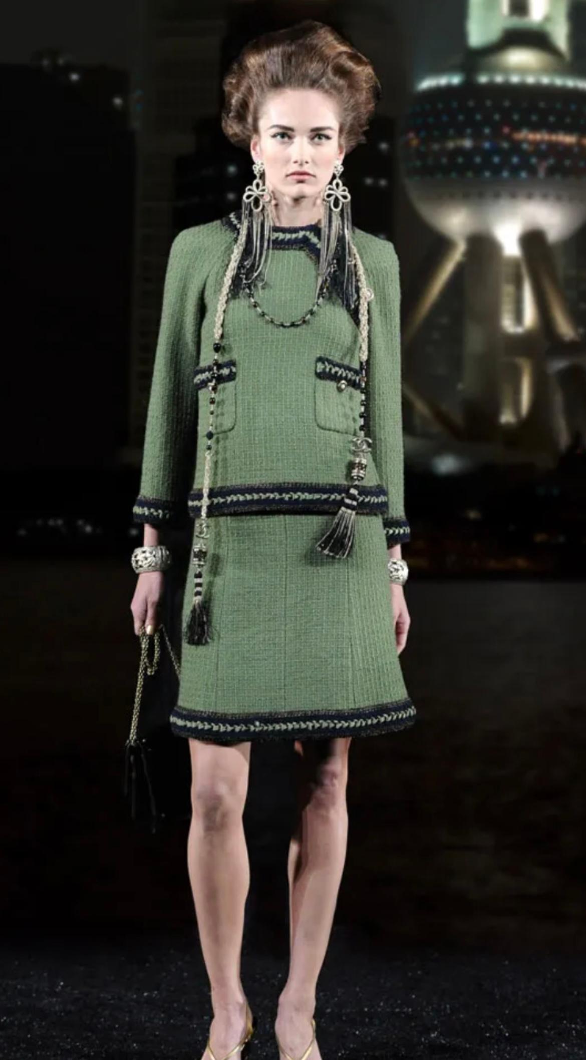 Iconic Chanel khaki green tweed suit from Ad Campaign of Paris / Shanghai Collection
Size mark 38 FR. Condition is pristine.
- CC logo ancient 'coin' buttons
- tonal silk lining with camellias, chain link at hem