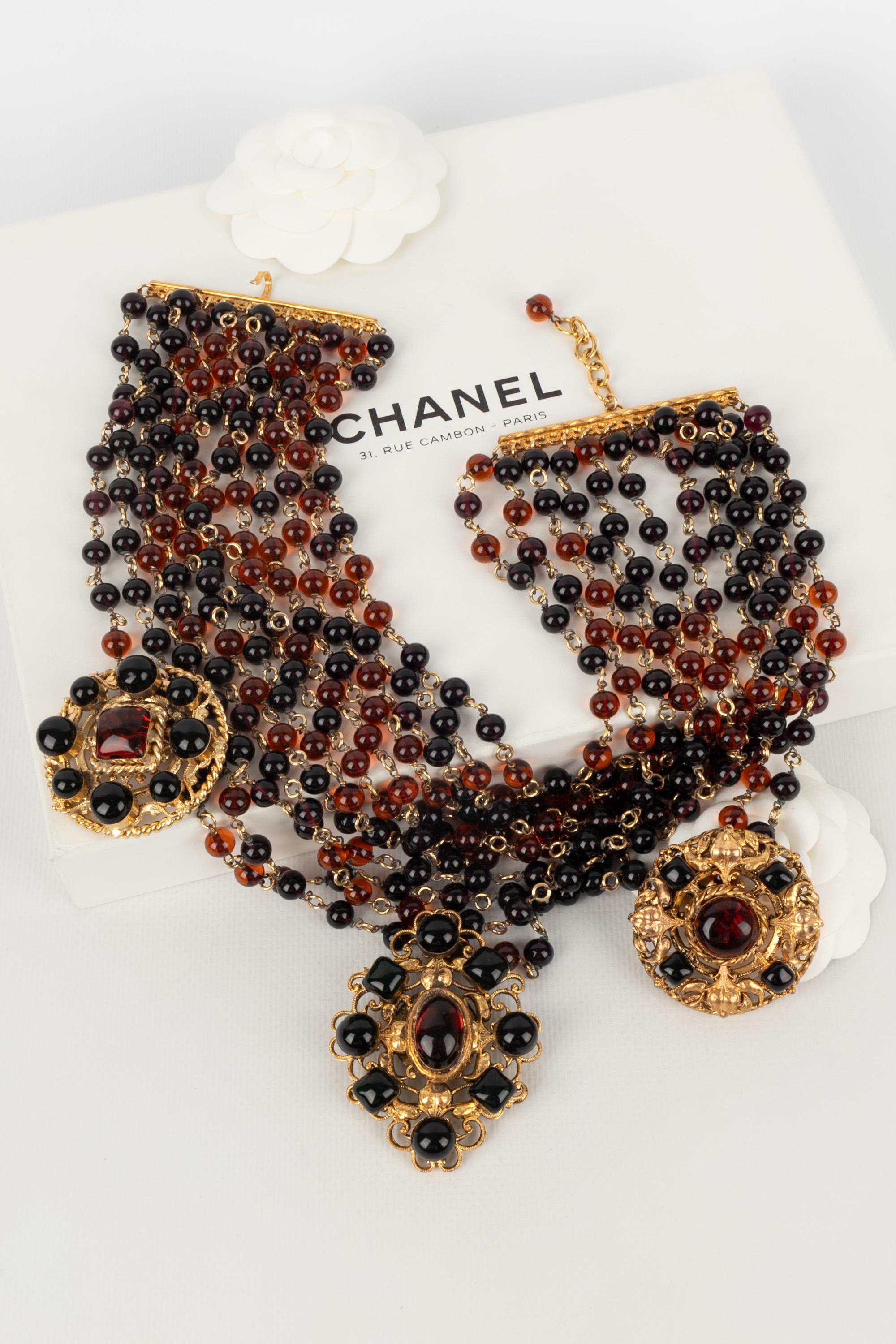 CHANEL - (Fabriqué en France) Impressionnant collier dickey avec de multiples rangs de perles de verre dans les tons violets et bruns. Il est accompagné de trois pendentifs en métal doré et d'un pendentif en pâte de verre.

Condit :
Très bon