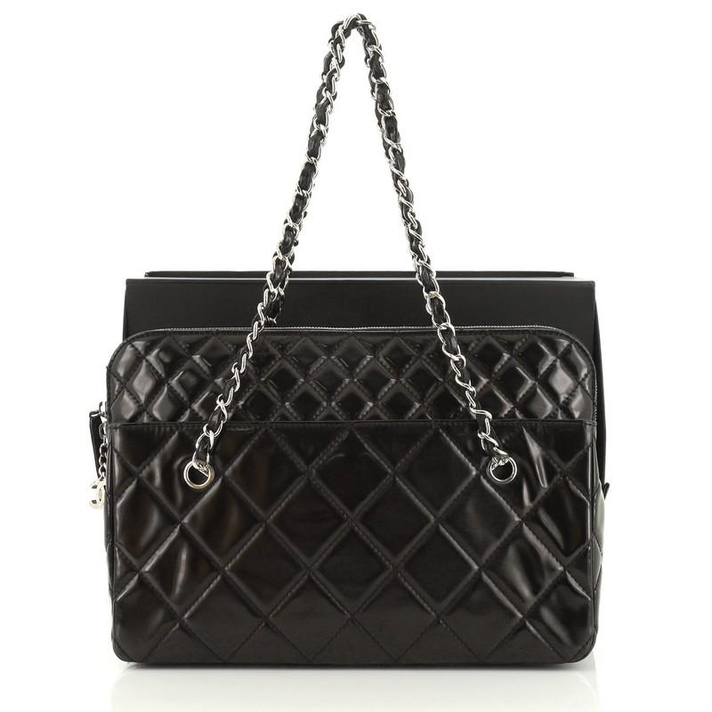 This Chanel In The Business Camera Bag Quilted Patent Vinyl Large, crafted from black quilted patent vinyl, features woven in leather chain straps, exterior front and back pockets, and silver-tone hardware. Its zip closure opens to a black fabric
