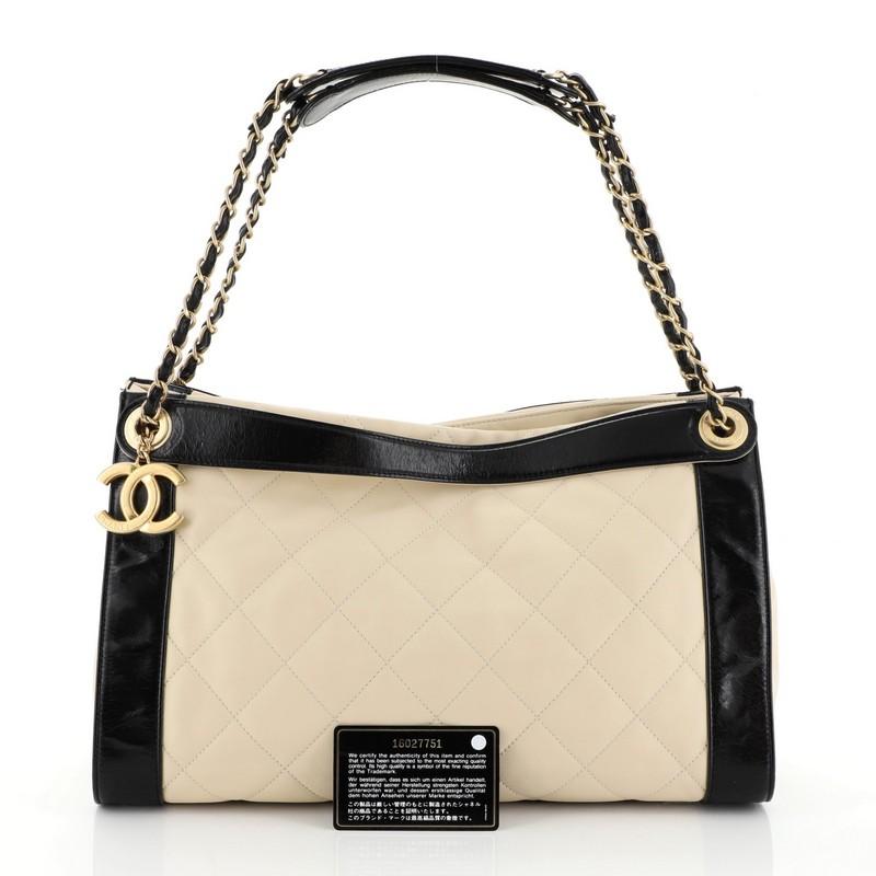 This Chanel In the Mix Charm Tote Quilted Leather Medium, crafted from black and neutral quilted leather, features dual flat leather handles, dual woven-in leather chain straps, and gold-tone hardware. It opens to a neutral fabric interior. Hologram