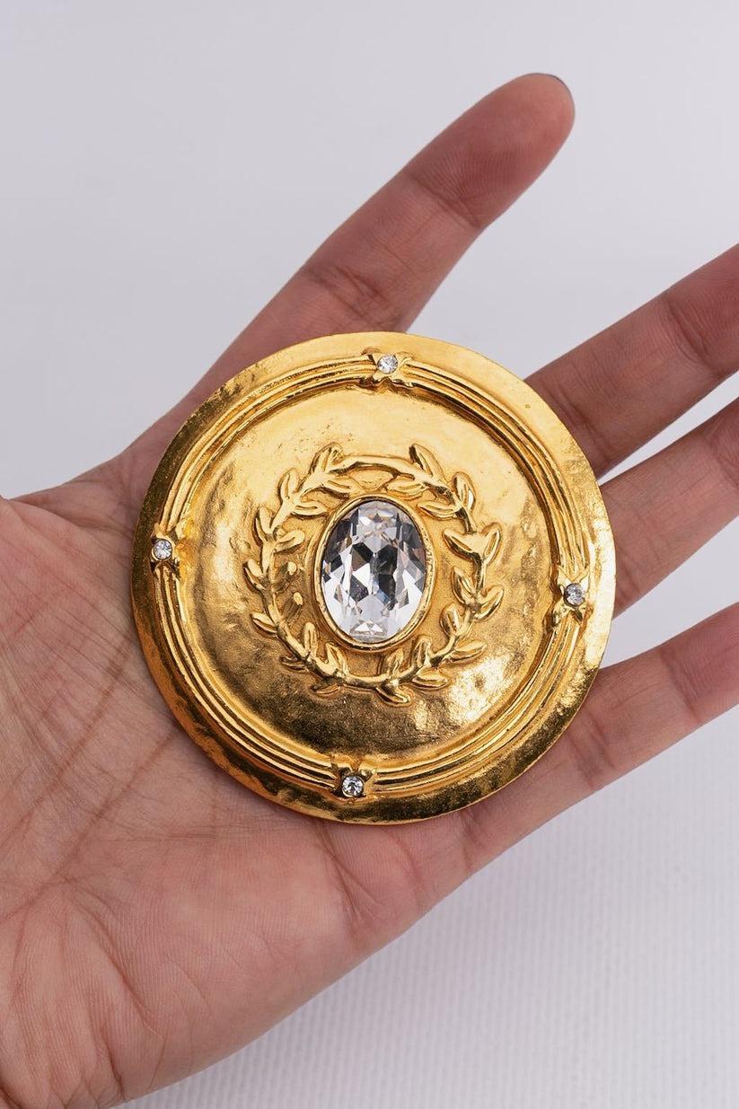 Chanel - (Made in France) Round brooch in gilded metal decorated with rhinestones, representing branches in its center.

Additional information:
Condition: Very good condition
Dimensions: Diameter: 6 cm (2.36