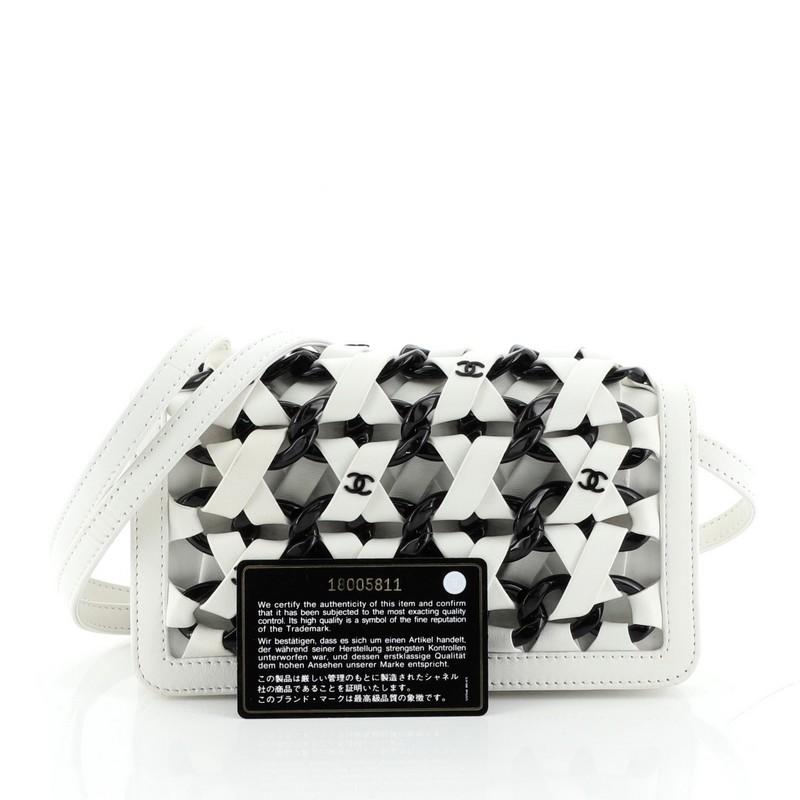 This Chanel Interlaced Chain Strap Clutch Braided Leather and Resin Mini, crafted in white and black leather, features a leather strap, acetate chains woven in the body, CC logos and gunmetal-tone hardware. It opens to a black fabric interior with