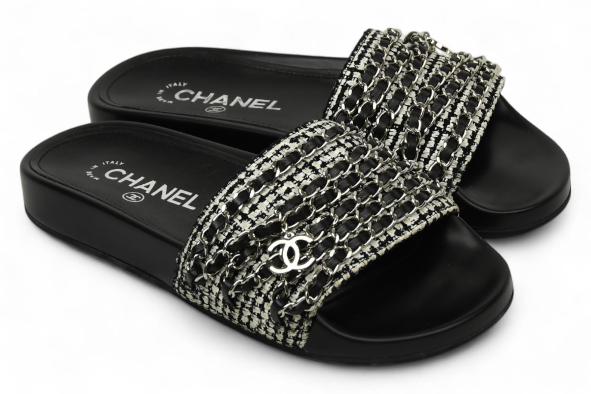 Effortlessly chic and unmistakably Chanel, these black slides feature the house’s signature tweed interwoven with gleaming silver chain accents, creating a modern, textured finish. The iconic interlocking CC logo adorns the vamp, adding an instantly