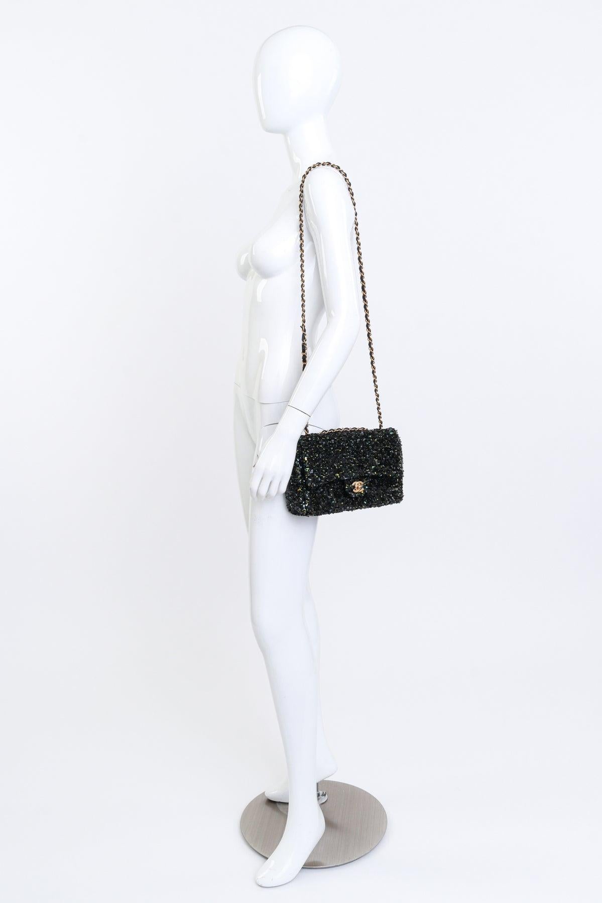 Este bolso Chanel está hecho de lentejuelas iridiscentes en negro, dorado, azul y verde, que crean un efecto dinámico y brillante. Lleva una bandolera ajustable de cadena entretejida en piel y una solapa delantera sujeta con un cierre de giro CC. El